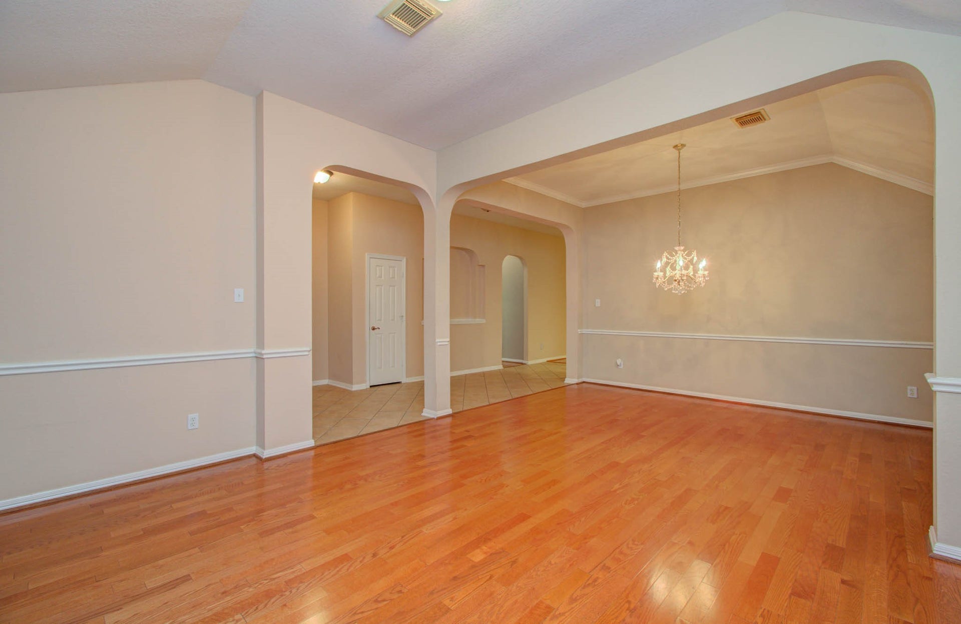 14403 Red Tailed Hawk Lane, Houston, TX 77044 Elegant open-concept living space with warm wood flooring, arched entryways, and a sparkling chandelier, perfect for entertaining.