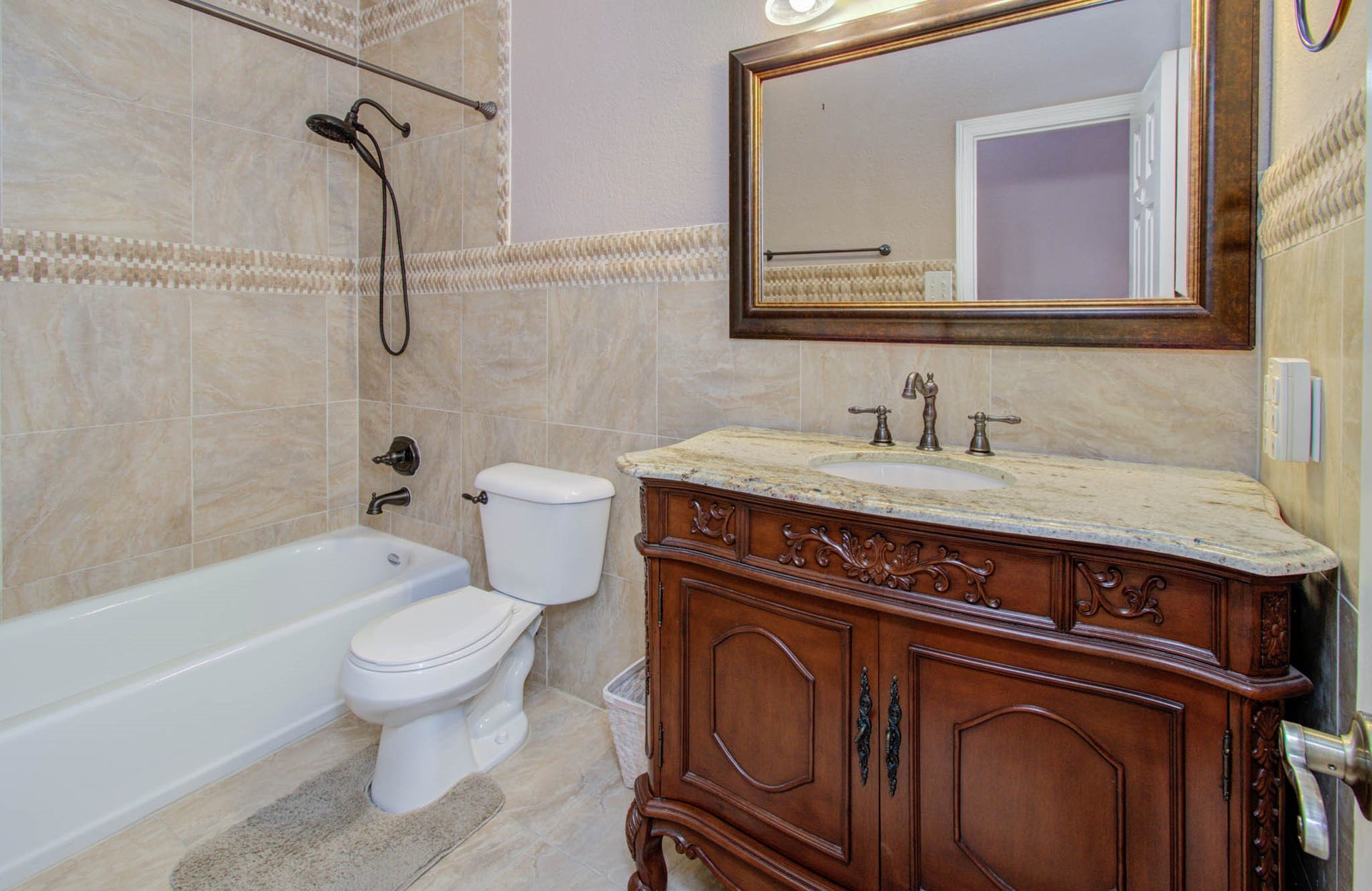 14403 Red Tailed Hawk Lane, Houston, TX 77044 Elegant bathroom featuring a luxurious granite-topped vanity with ornate wood detailing, complemented by a stylish tiled shower and bath.