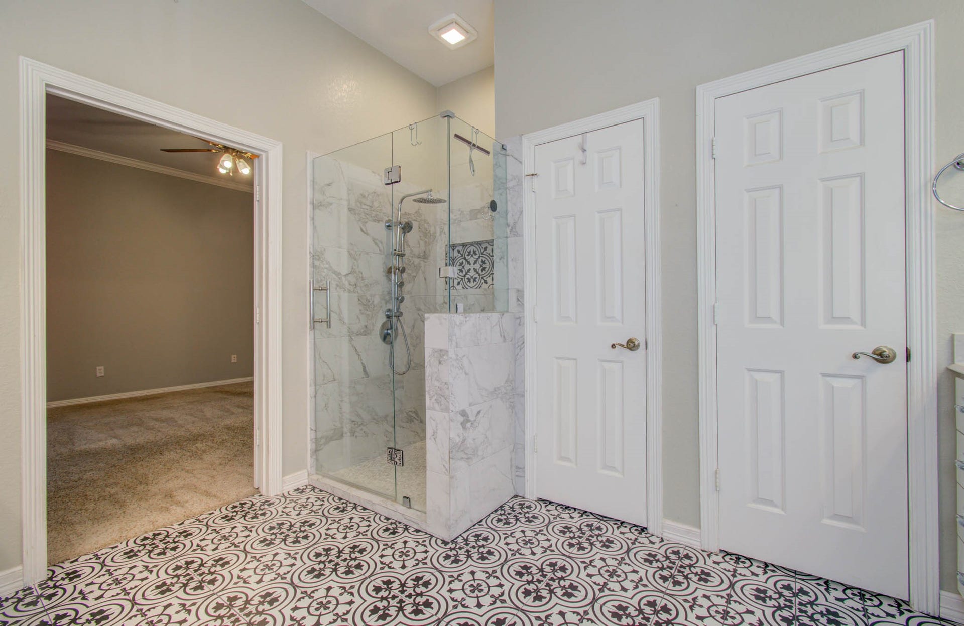 14403 Red Tailed Hawk Lane, Houston, TX 77044 Elegant bathroom featuring a luxurious glass-enclosed marble shower and stylish patterned tile flooring, with convenient access to an adjoining carpeted room.