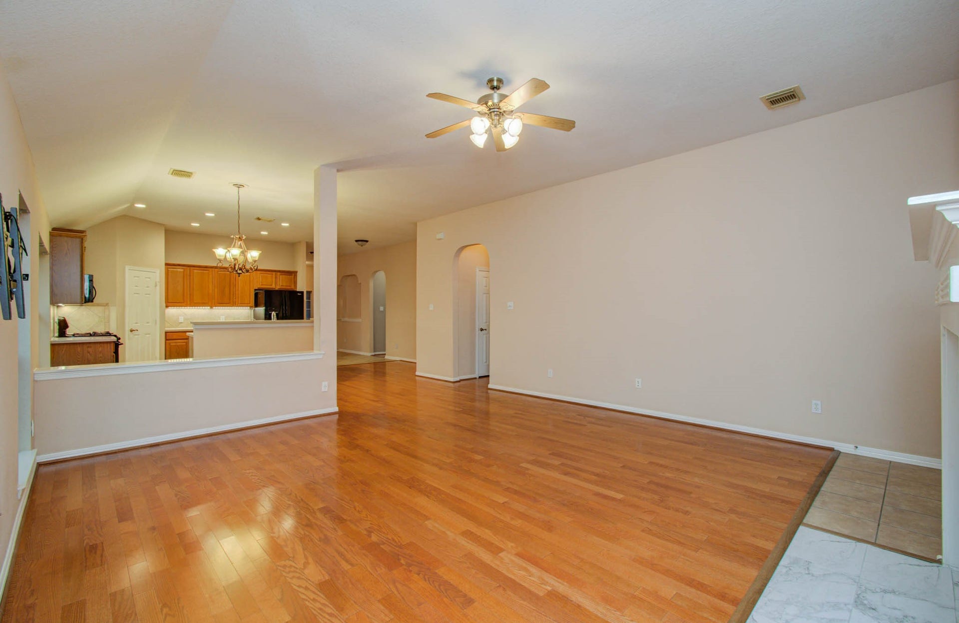 14403 Red Tailed Hawk Lane, Houston, TX 77044 Spacious living area with warm hardwood floors, high ceilings, and a ceiling fan, seamlessly flowing into an inviting kitchen with modern lighting and ample cabinetry.