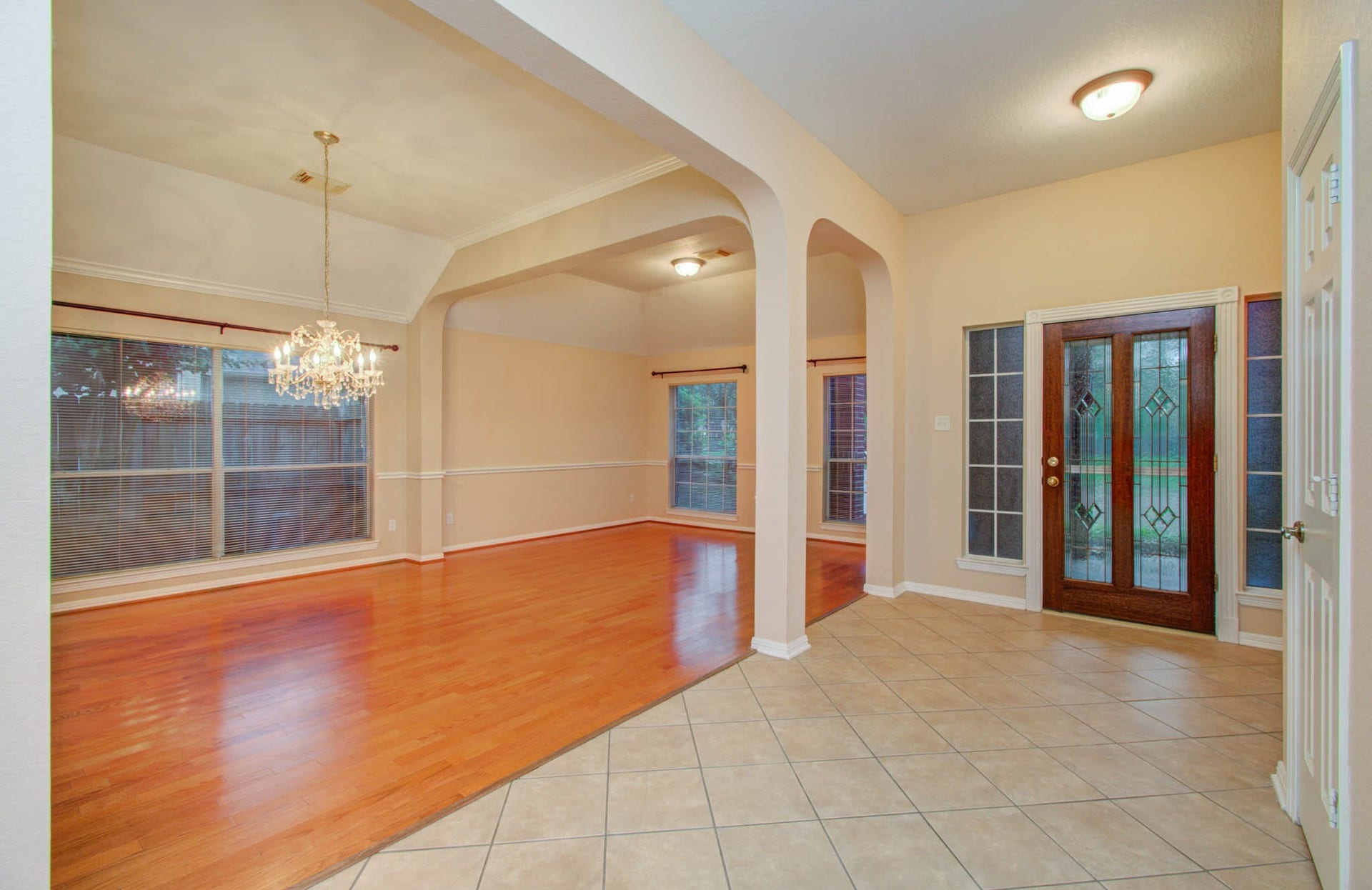 14403 Red Tailed Hawk Lane, Houston, TX 77044 Elegant entryway with a tiled floor and decorative glass door leads to a spacious living area featuring warm wood flooring and a sparkling chandelier, perfect for entertaining.