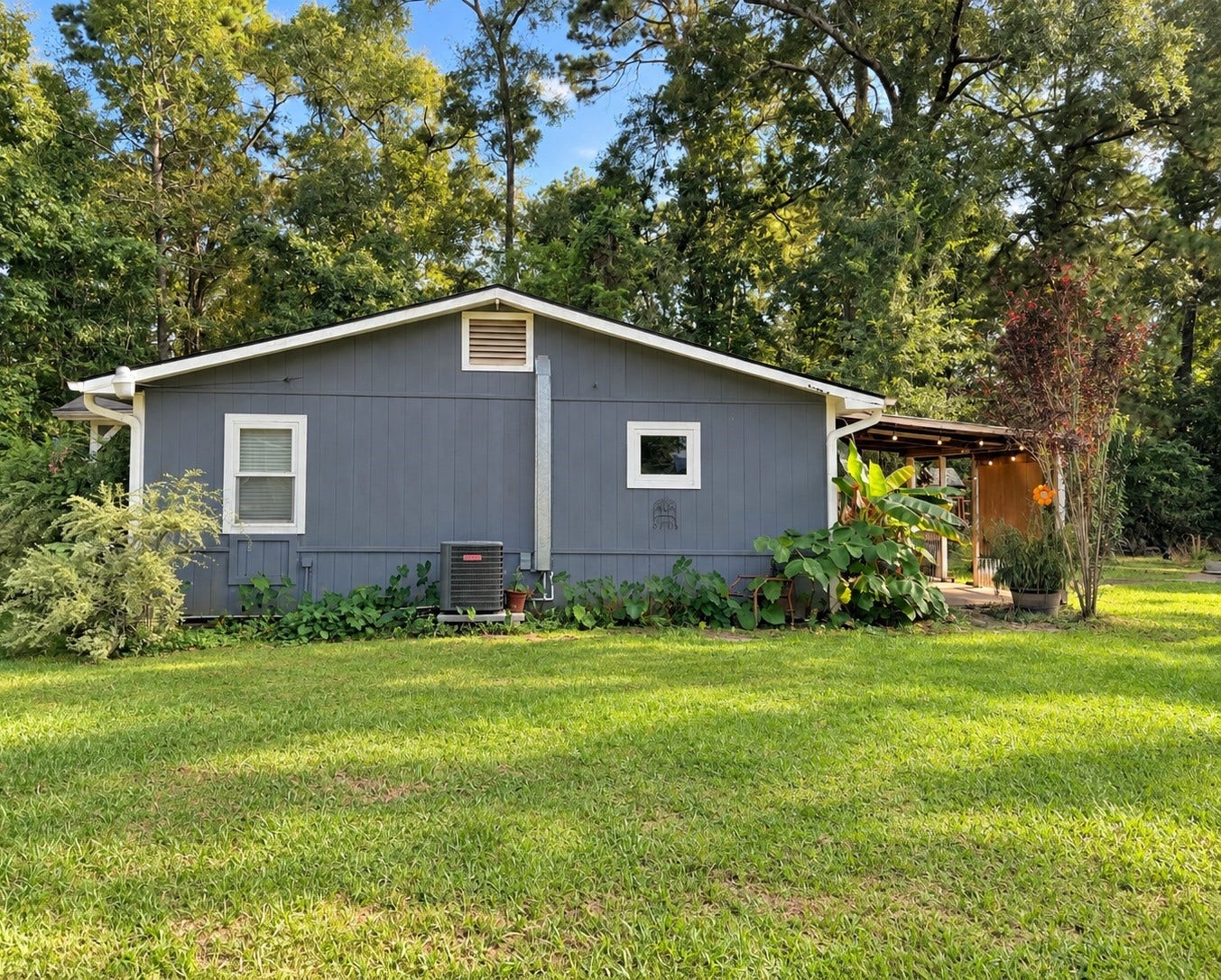 14440 Lakecrest Drive, Splendora, TX 77372 Rear/Side Exterior Side exterior with mature landscaping, covered outdoor area and expansive grassy yard.