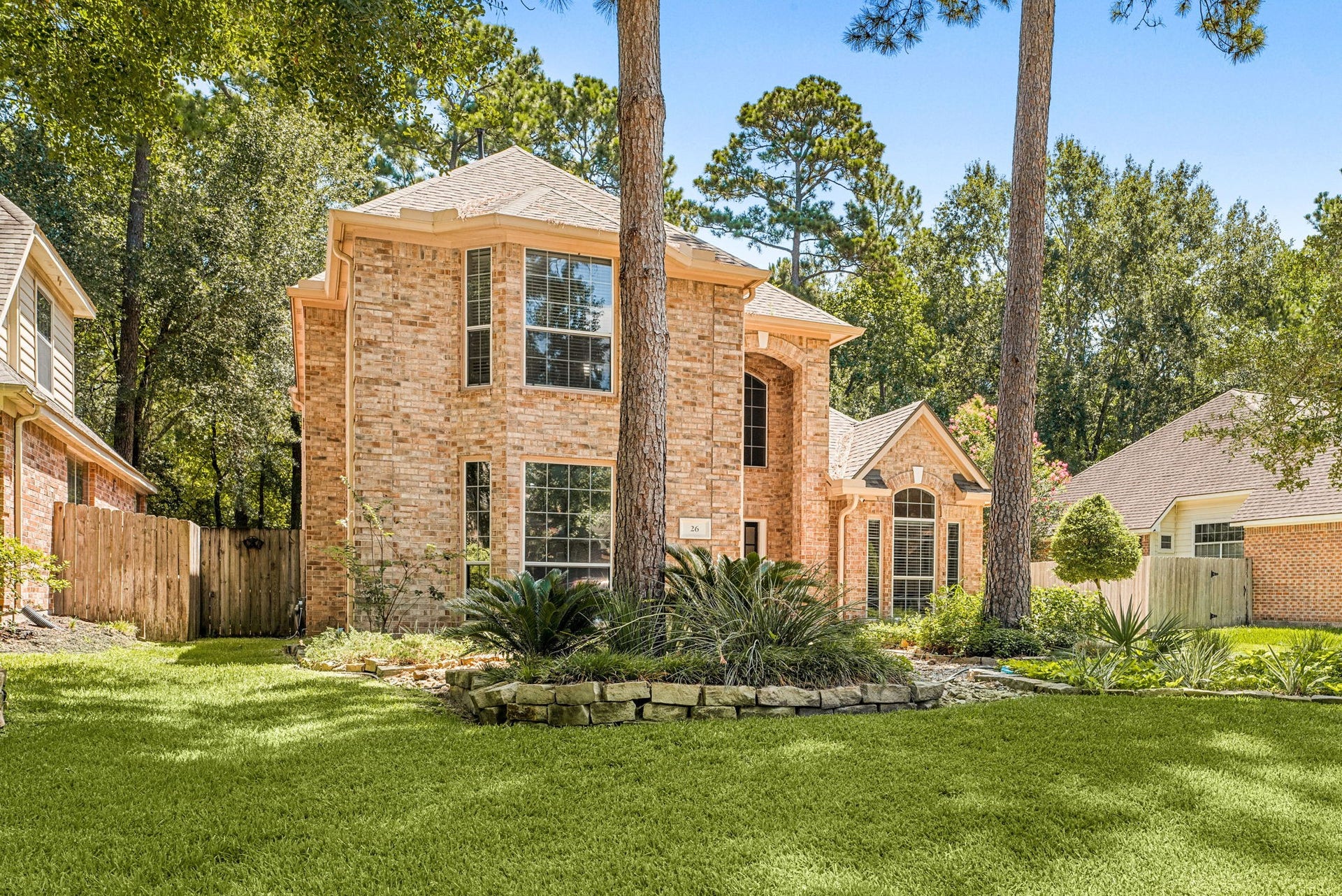 26 Cinnamon Teal Place, The Woodlands, TX 77382 brick home with elegant arched windows, nestled among mature trees and lush landscaping.