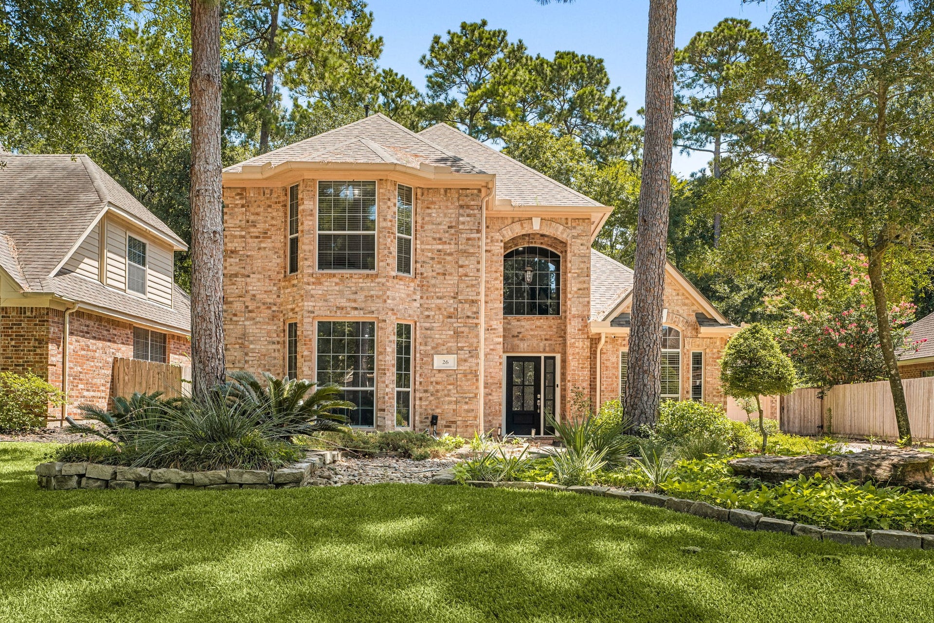 26 Cinnamon Teal Place, The Woodlands, TX 77382 Stunning two-story brick home with elegant arched windows, nestled among mature trees and lush landscaping.