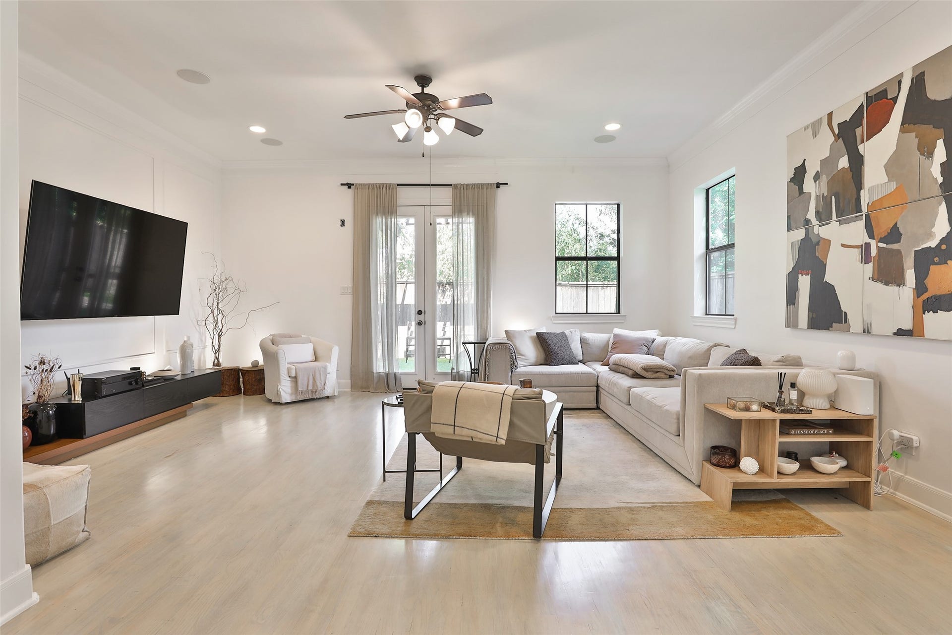 1112 Bingham Street, Houston, TX 77007 Bright and inviting living room featuring a modern sectional sofa, large wall-mounted TV, and stylish artwork, complemented by natural light from generous windows and glass doors.