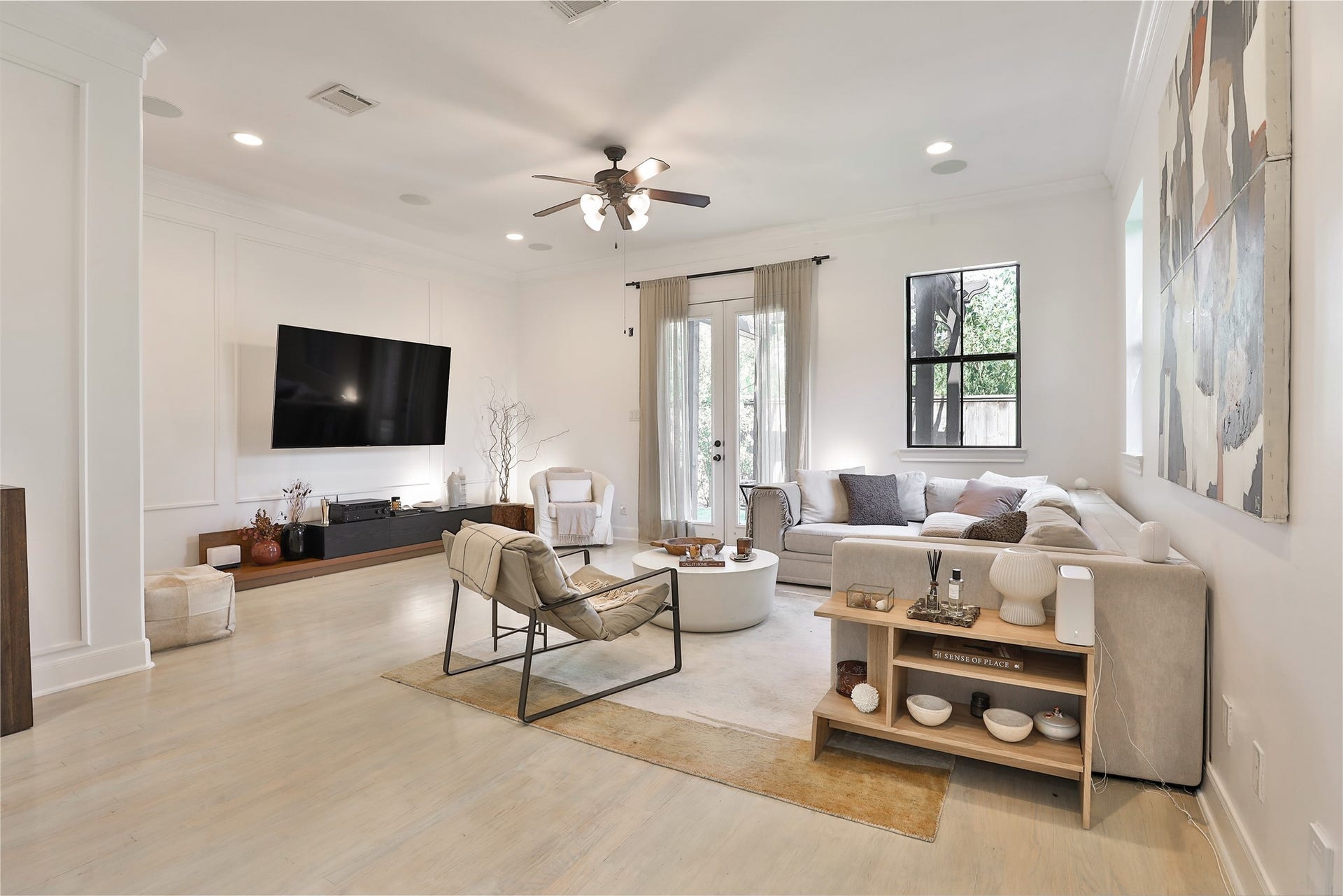 1112 Bingham Street, Houston, TX 77007 Spacious and modern living room featuring a sleek, wall-mounted TV, comfortable sectional sofa, and stylish accent chairs. Natural light pours in through large windows and glass doors, enhancing the airy ambiance.