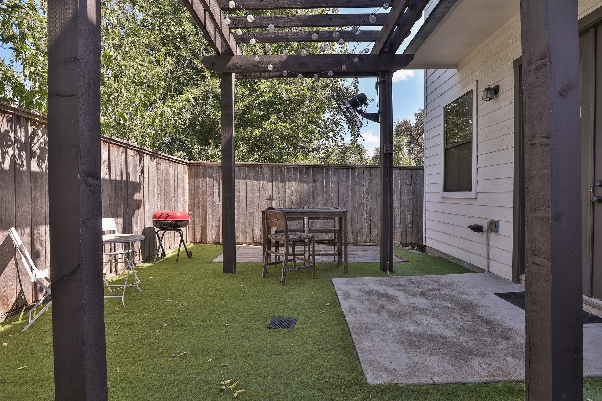 1112 Bingham Street, Houston, TX 77007 Charming backyard retreat featuring a cozy pergola, perfect for outdoor dining and relaxation, with a mix of artificial grass and concrete patio space.