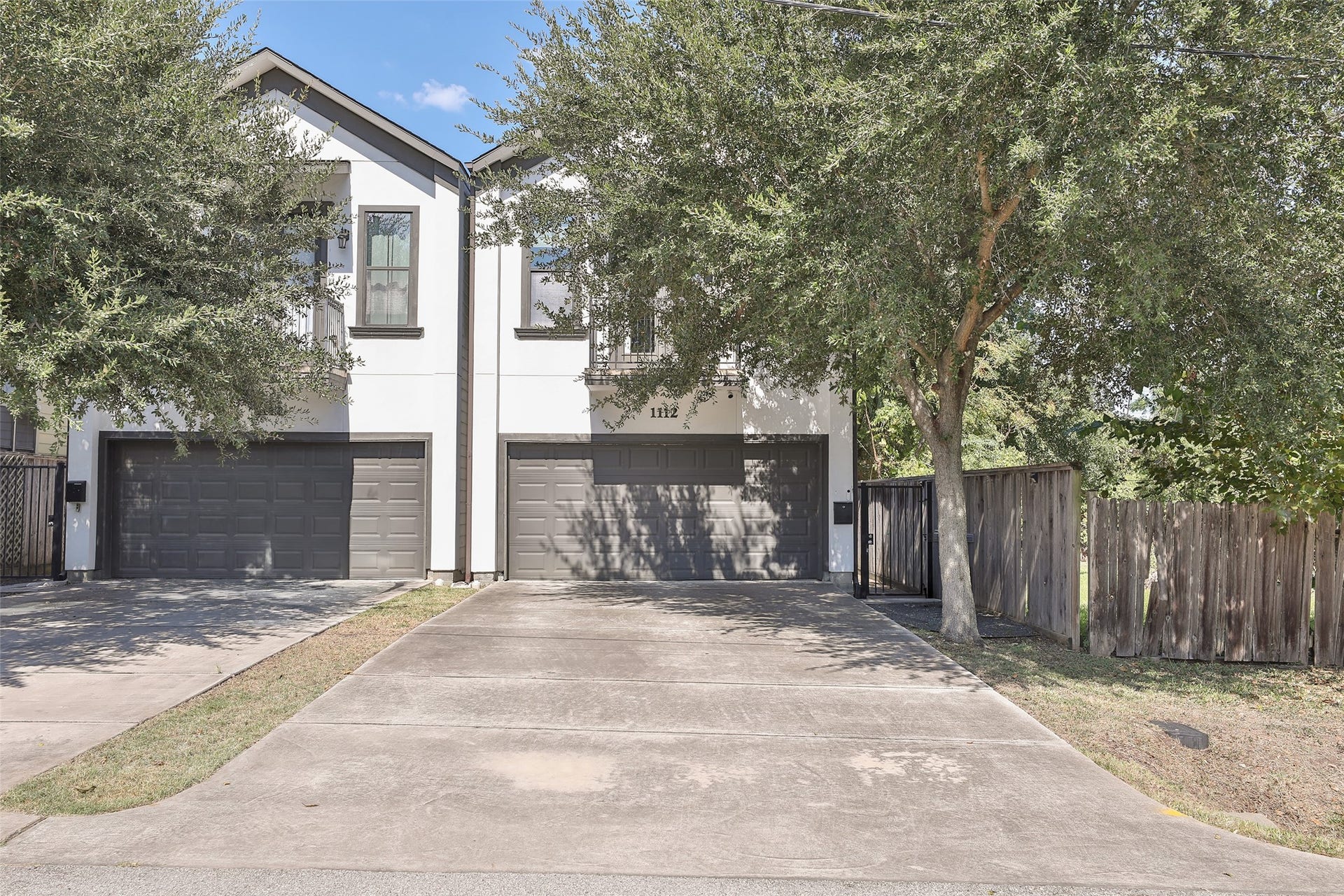 1112 Bingham Street, Houston, TX 77007 Modern duplex with sleek design features dual garages and a spacious driveway, framed by lush trees and a privacy fence.