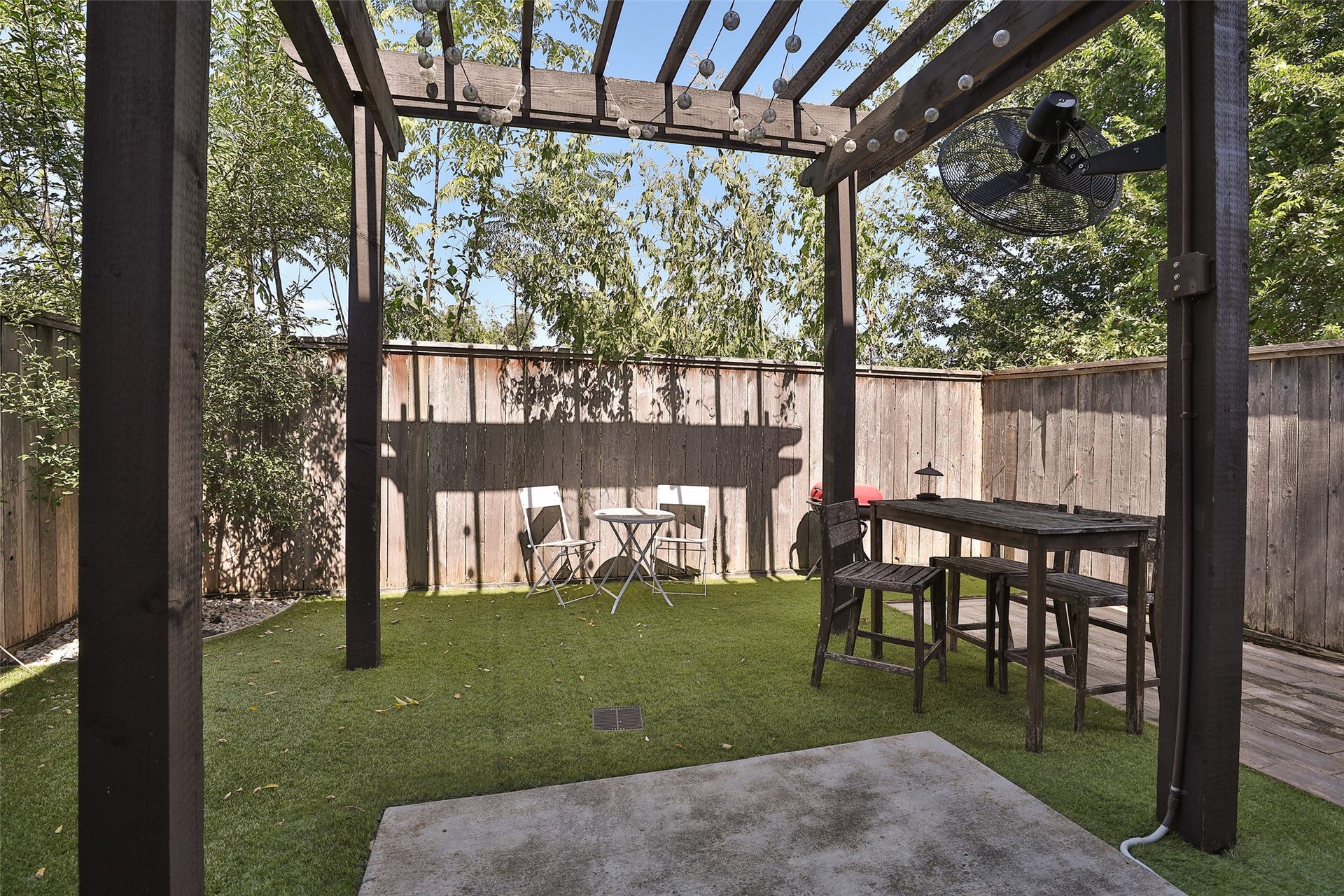 1112 Bingham Street, Houston, TX 77007 Charming backyard retreat featuring a pergola with string lights, lush artificial grass, and cozy seating, perfect for outdoor dining and relaxation.