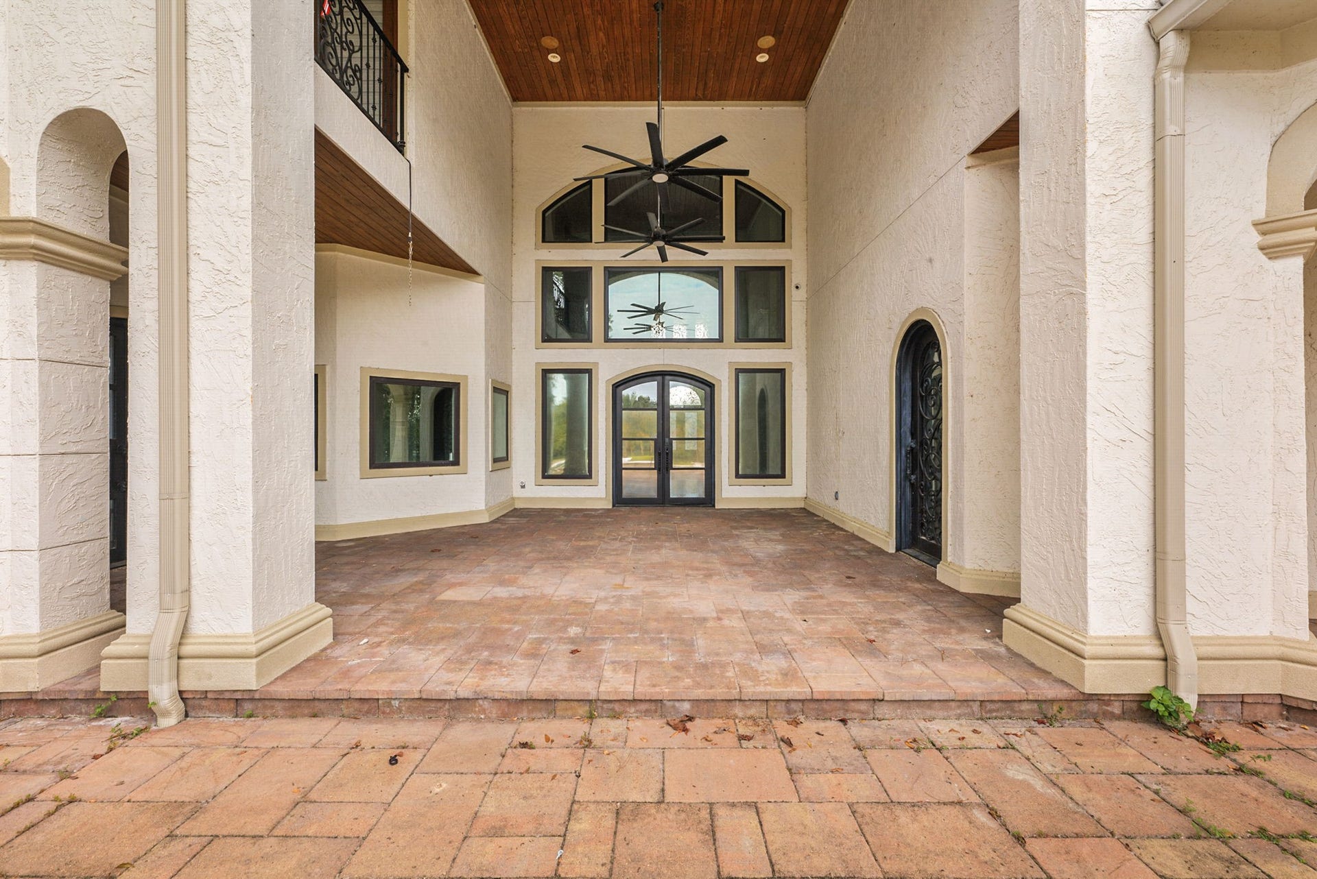 Make an unforgettable first impression with this grand, multi-story covered entryway. The majestic front porch features towering columns, elegant tile flooring, and a warm wood-plank ceiling complete with an outdoor fan. A magnificent wall of windows and glass-paneled double doors floods the interior with natural light while hinting at the luxury that lies within.
