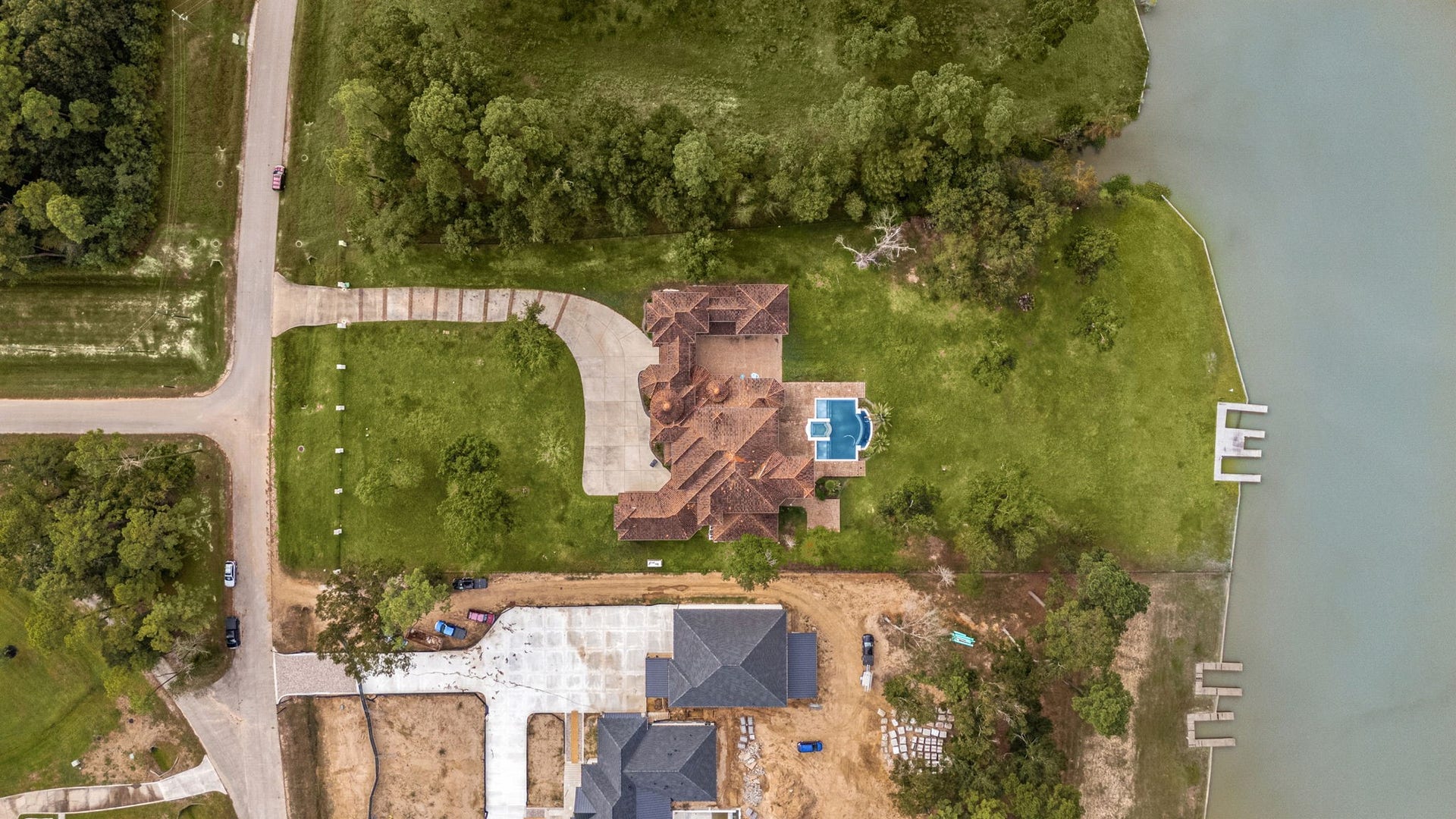 An birds-eye satellite perspective captures the ultimate lakefront footprint of this estate. The layout highlights the grand motor court and long private driveway leading from the street, opening up to an expansive, lush green lawn that flows past the resort-style pool straight to the water's edge. Anchored by private dock access and bordered by dense, mature trees, this unique lot offers a rare combination of acreage, privacy, and true waterfront living.