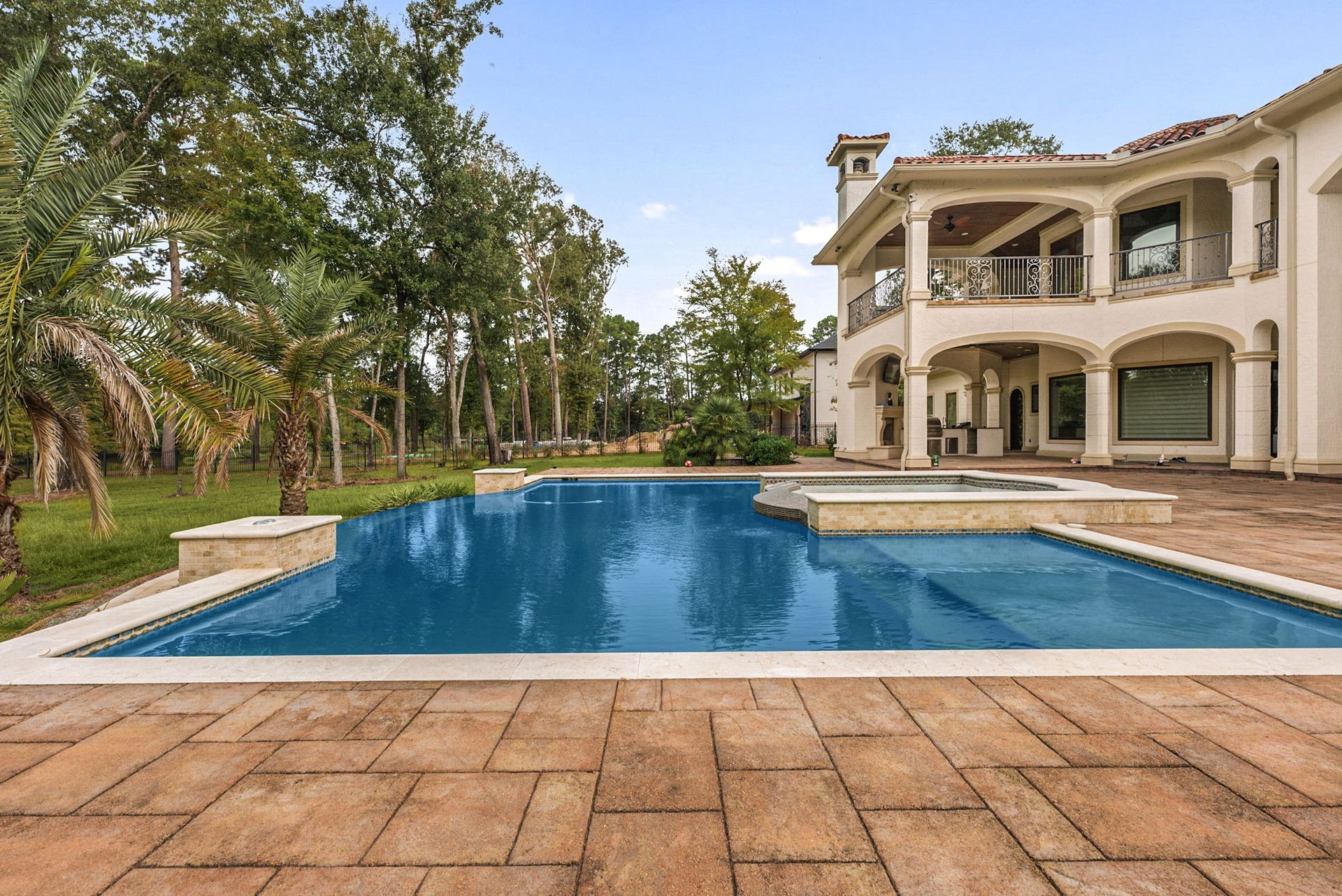 Escape to your own private resort with this sparkling swimming pool and elevated spa. Framed by a sprawling brick-paver deck and a backdrop of towering, mature trees, this backyard sanctuary offers total tranquility. The homes striking dual-level covered patios look out over the deep blue water, creating a seamless connection between indoor luxury and outdoor relaxation.