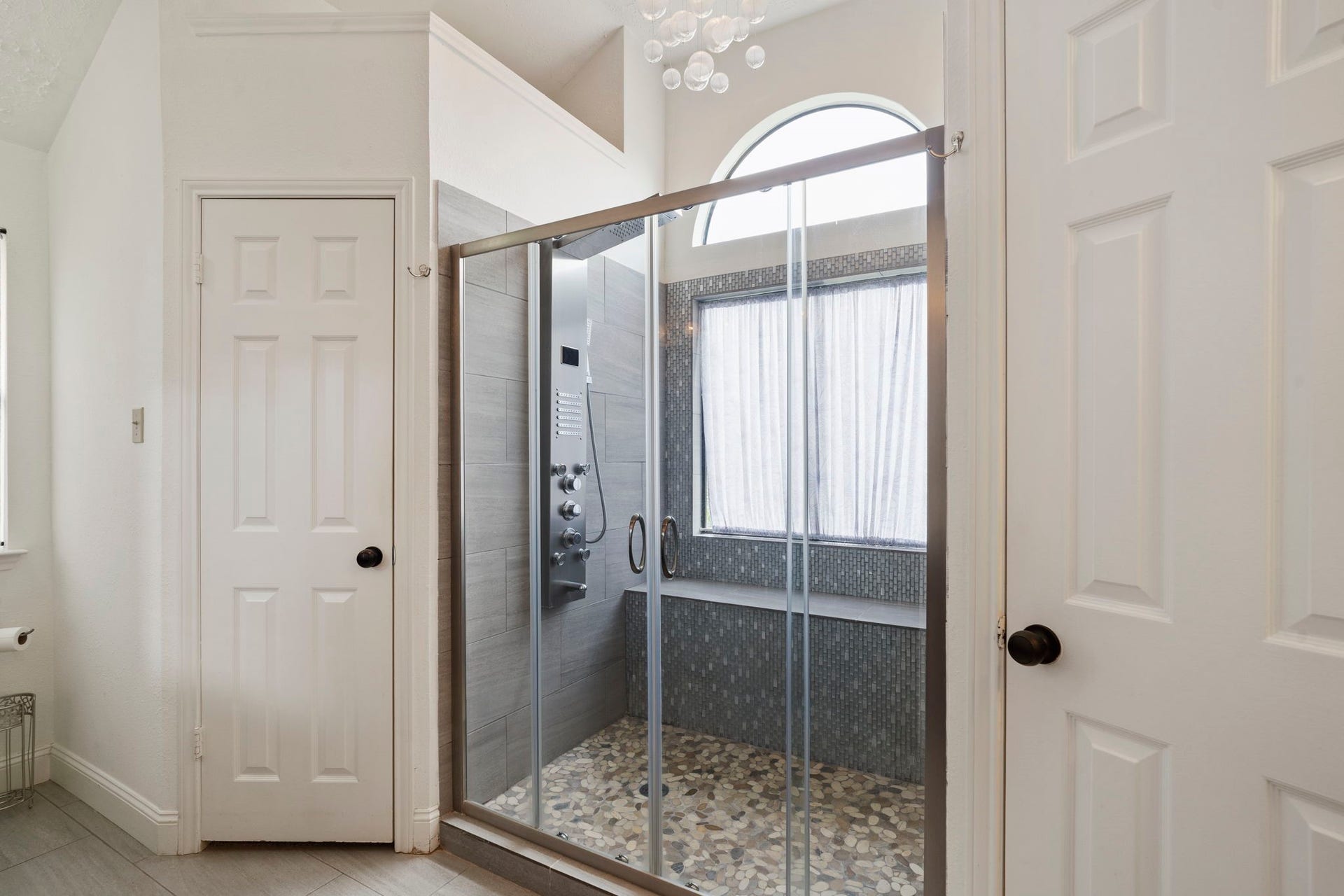 2437 Willow Bend Drive, Richmond, TX 77406 Luxurious bathroom featuring a spacious glass-enclosed shower with modern fixtures and a pebble stone floor, complemented by elegant tilework and abundant natural light from the arched window.