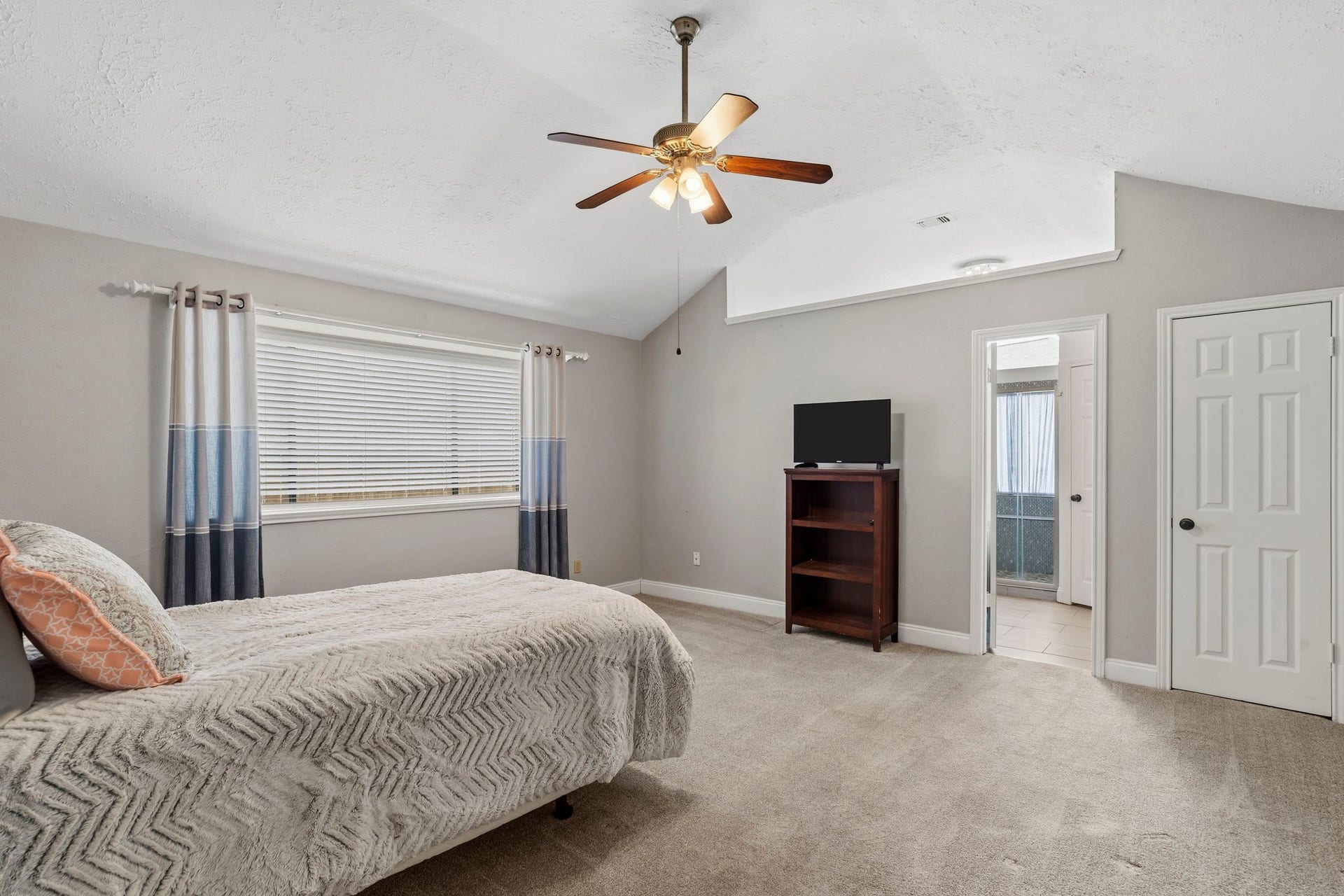2437 Willow Bend Drive, Richmond, TX 77406 Spacious primary bedroom with vaulted ceiling, ceiling fan, and neutral tones offers a cozy retreat. Ample natural light streams through a large window, and an ensuite bathroom adds convenience.