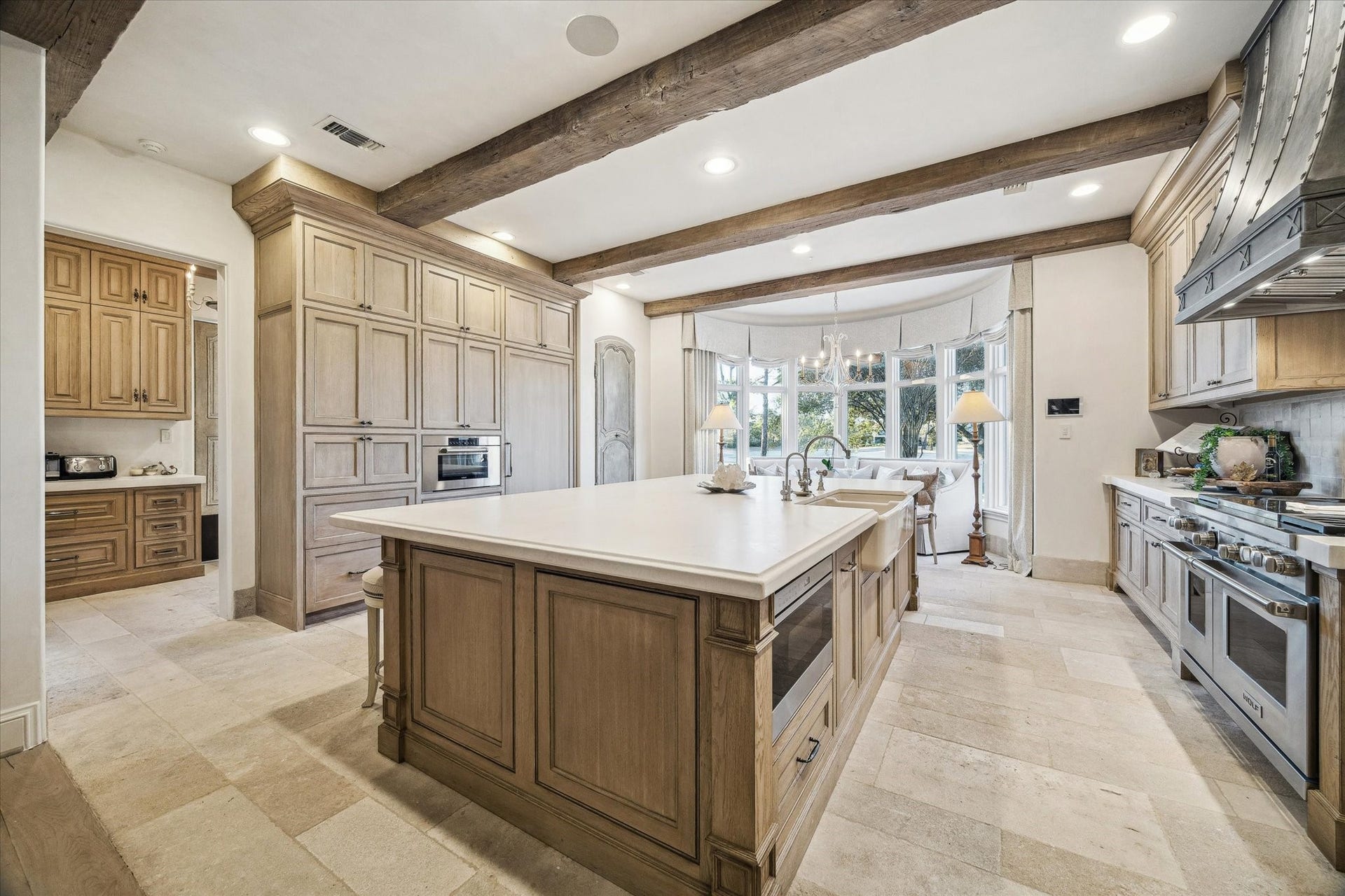Alternate view of the chef's kitchen highlighting the oversized island, custom cabinetry, walk-in pantry with imported door from Chateau Domingue, and premium appliances. Freezer drawers, fully paneled refrigerator, built in TV. Wolf Appliances.