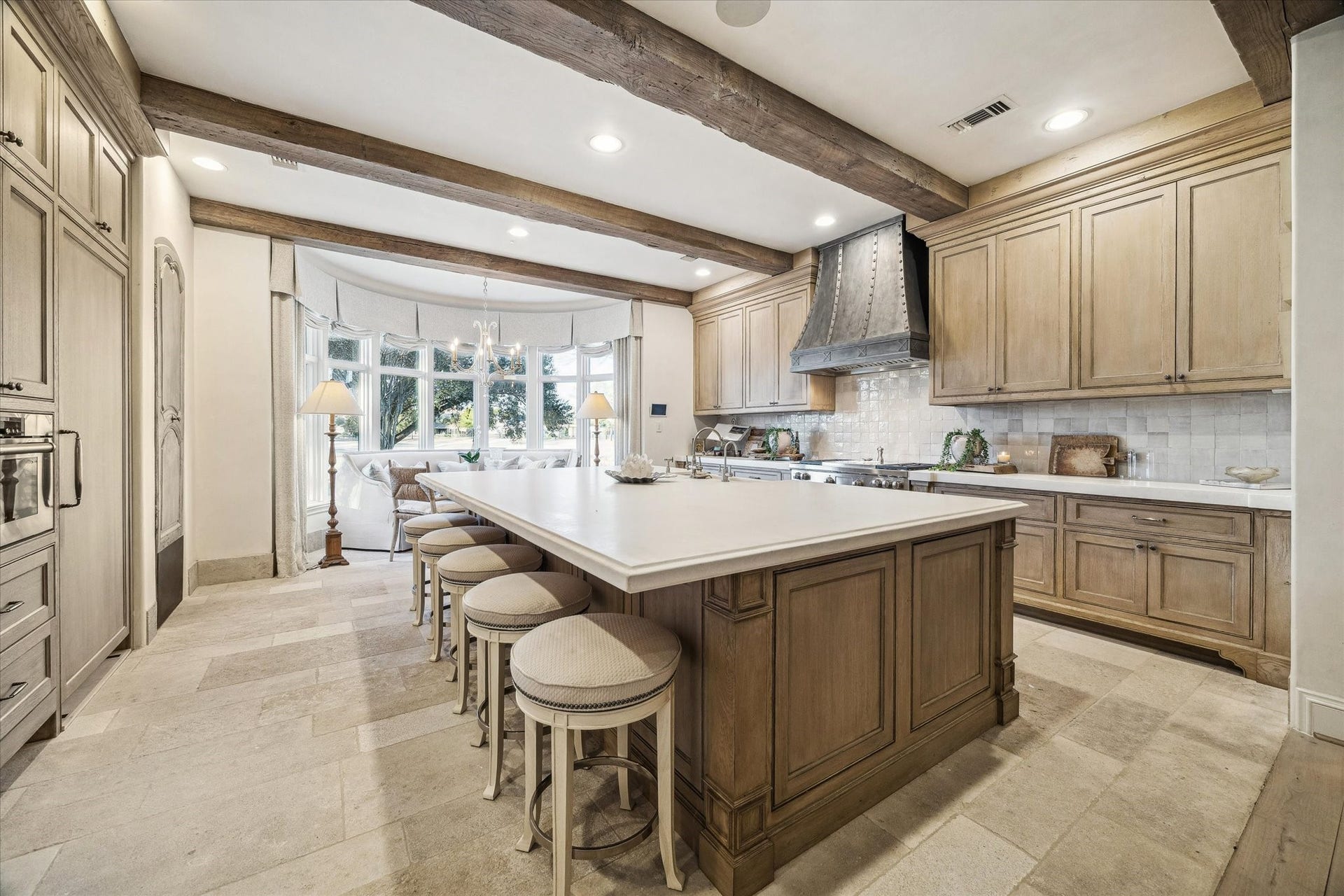 Chef's kitchen featuring a large center island with seating, custom white oak flush inset cabinetry, custom venthood, exposed antique wood beams, and high-end appliances. Beautiful limestone floors from Chateau Domingue.
