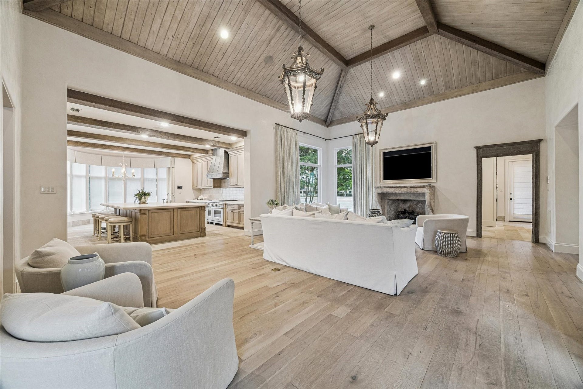 Spacious living room featuring vaulted ceilings with reclaimed wood beams, a fireplace with imported mid century surround, wood flooring, and an open layout connecting to the kitchen.