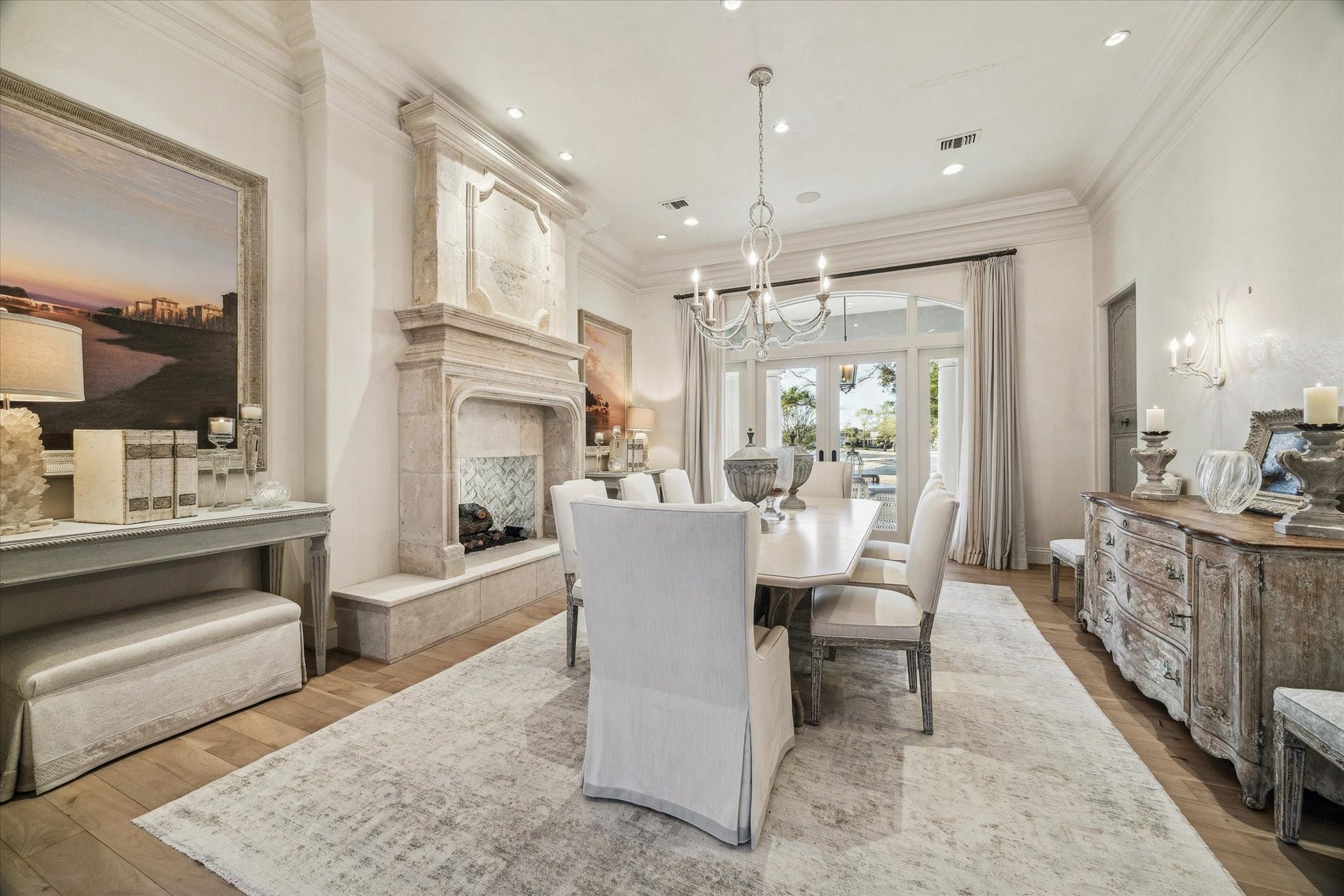 Formal dining room featuring a gorgeous imported mid century fireplace surround from France, elegant lighting, wood flooring, and french doors providing natural light and outdoor views.