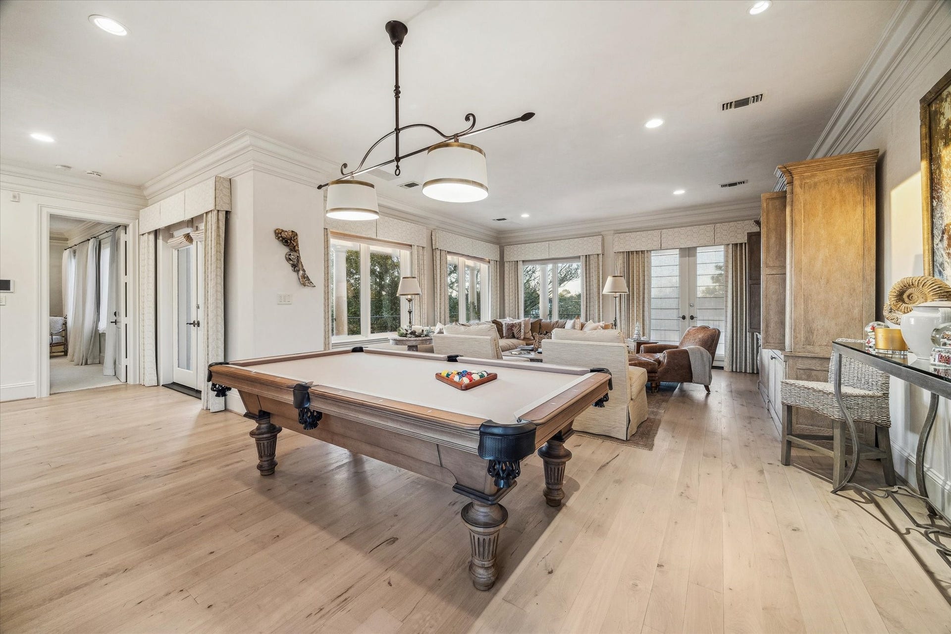 Game room with room for pool table, wood flooring, bar and seamless flow into a secondary living area.