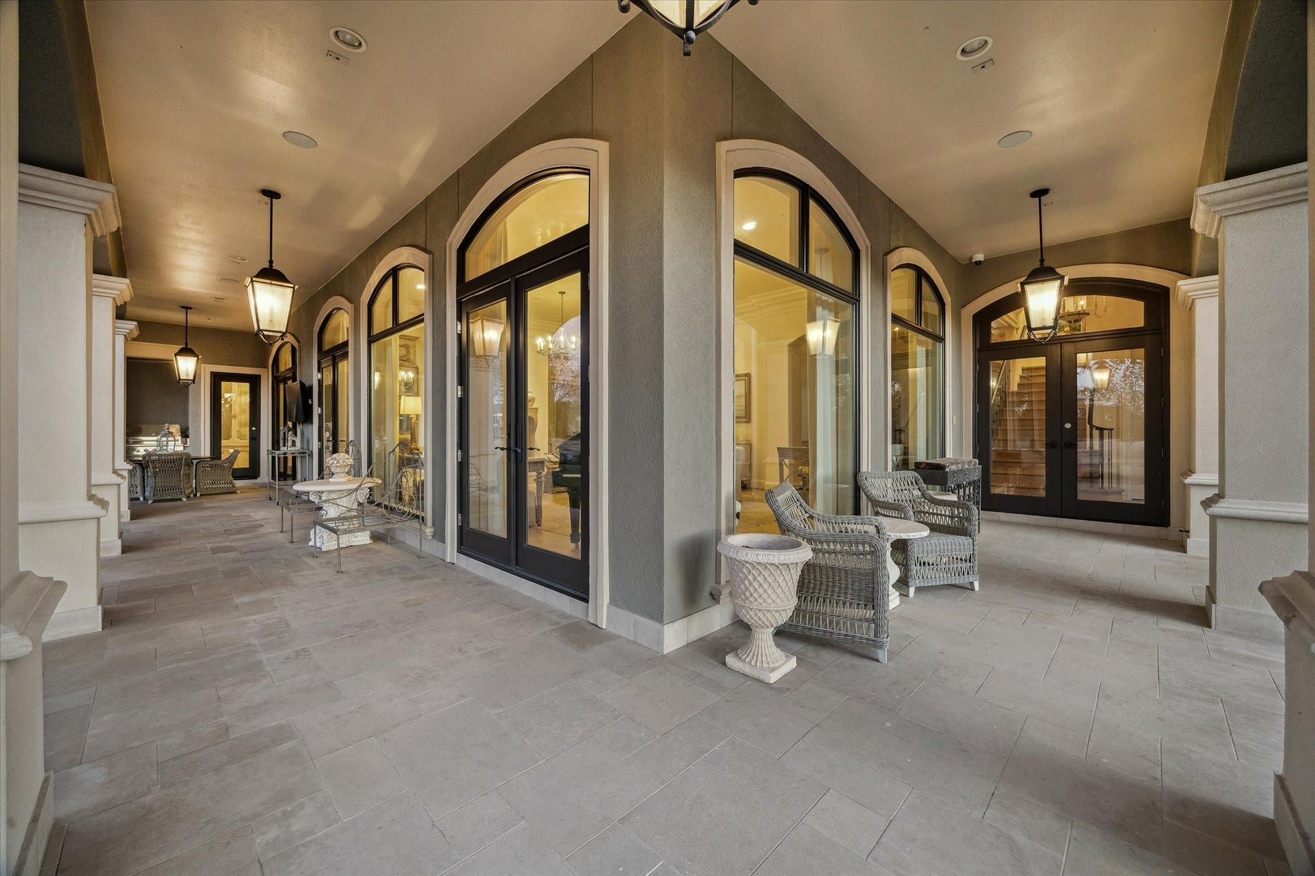 Wraparound covered patio with arched doors, stone flooring, and multiple seating areas offering seamless indoor-outdoor living.