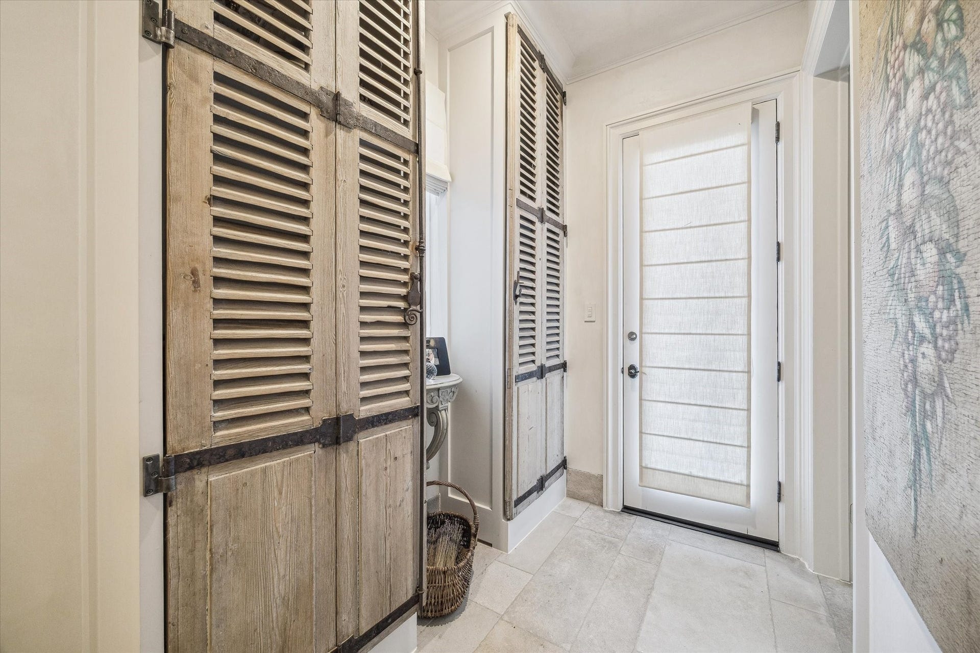 Mudroom-style side entry from garage featuring limestone flooring, custom louver doors, and convenient access to the laundry room, main living and kitchen areas.