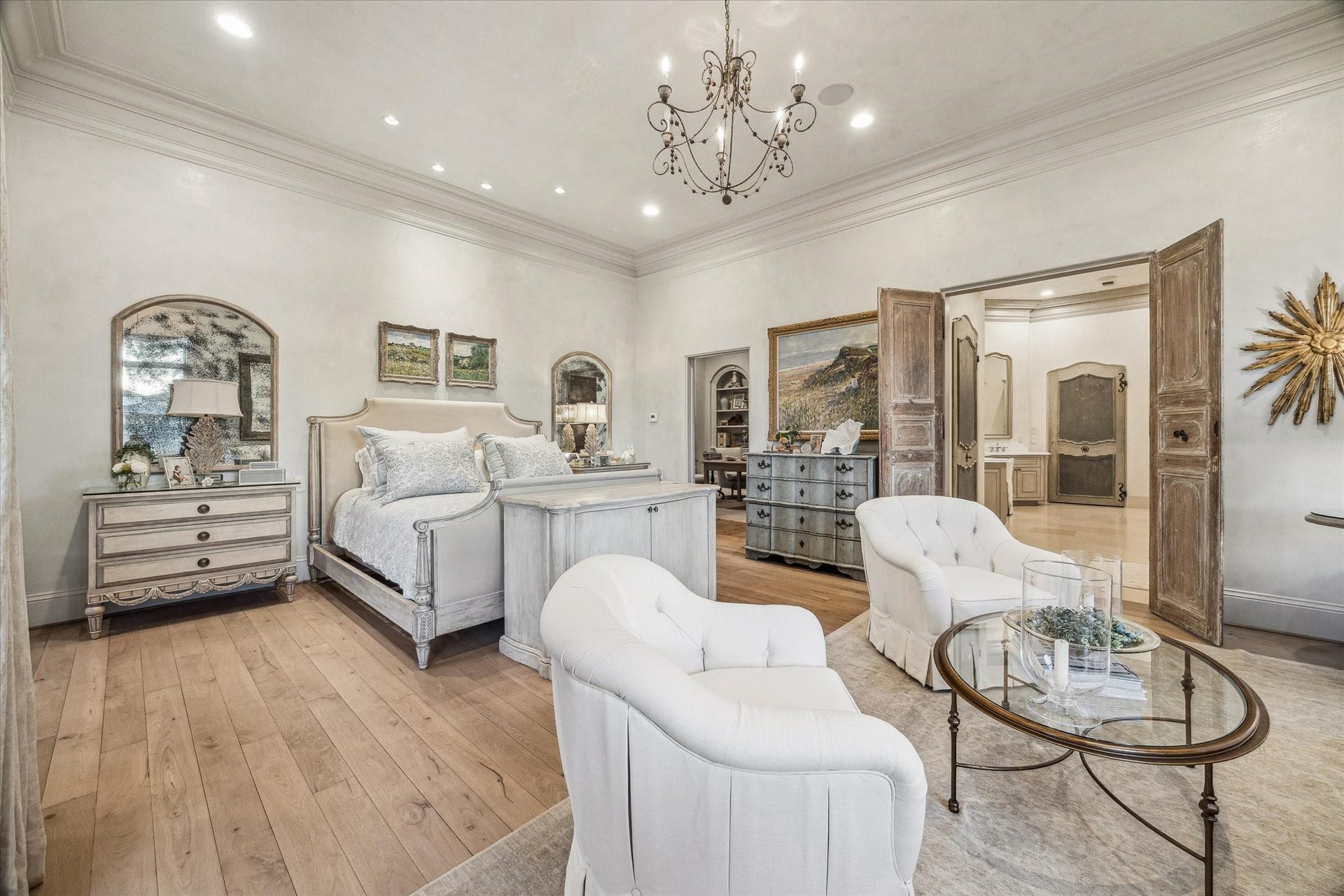 Alternate view of the primary bedroom highlighting generous space, wood flooring, elegant lighting, and direct access to the en suite bathroom.