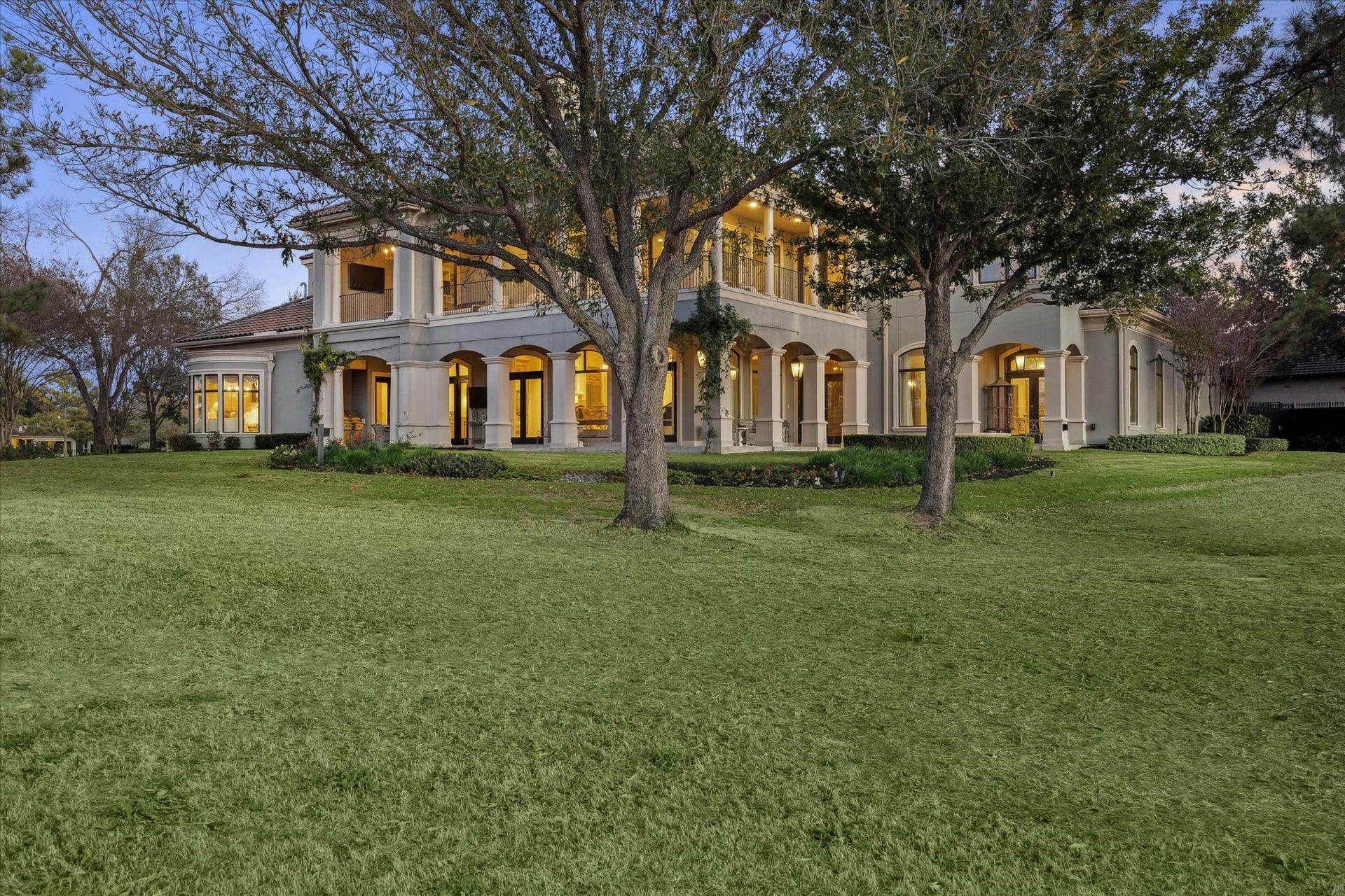 Rear exterior view highlighting expansive covered patios, upper-level balcony, and beautifully landscaped grounds.