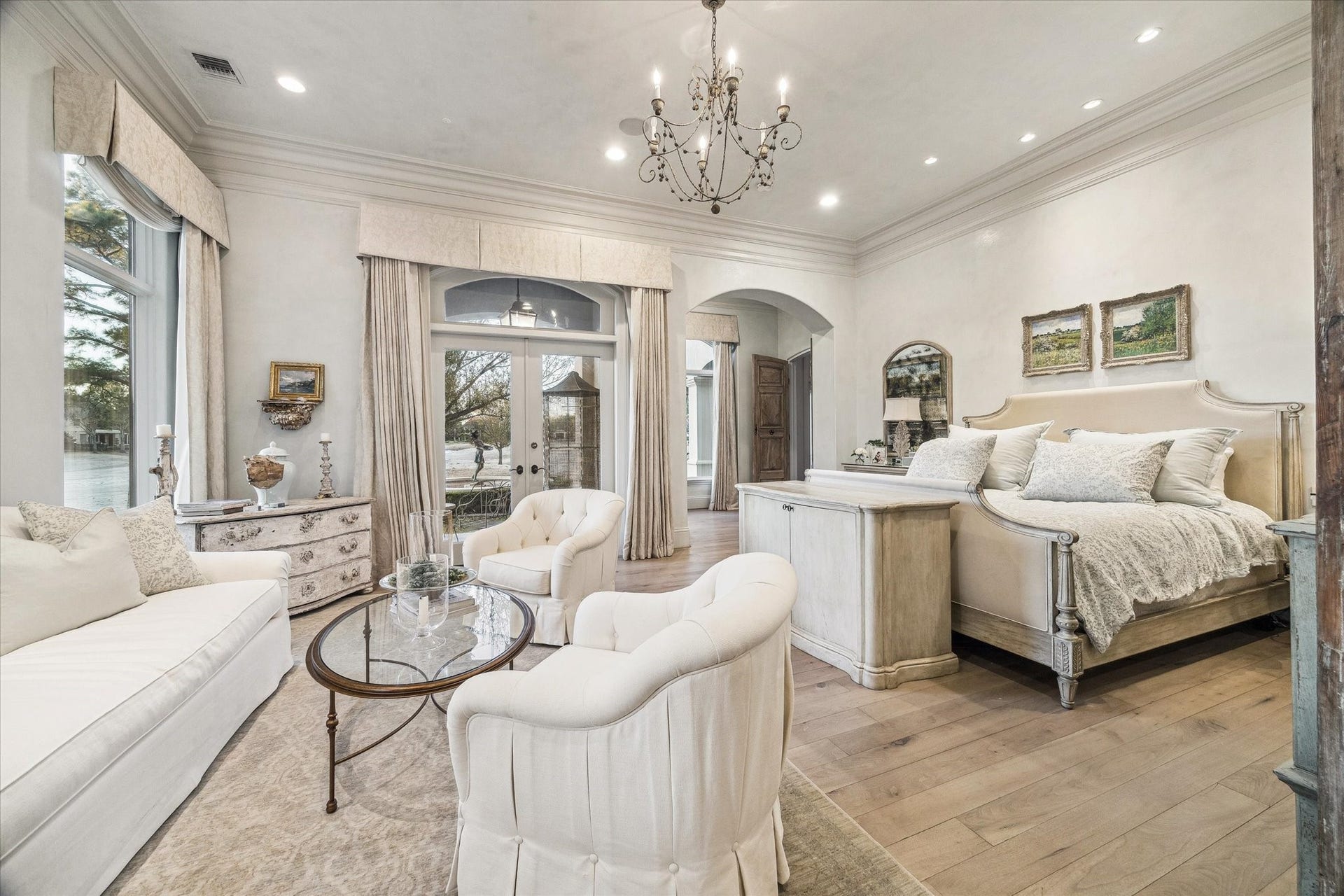 Primary bedroom featuring large windows, wood flooring, elegant lighting, and direct access to outdoor living.