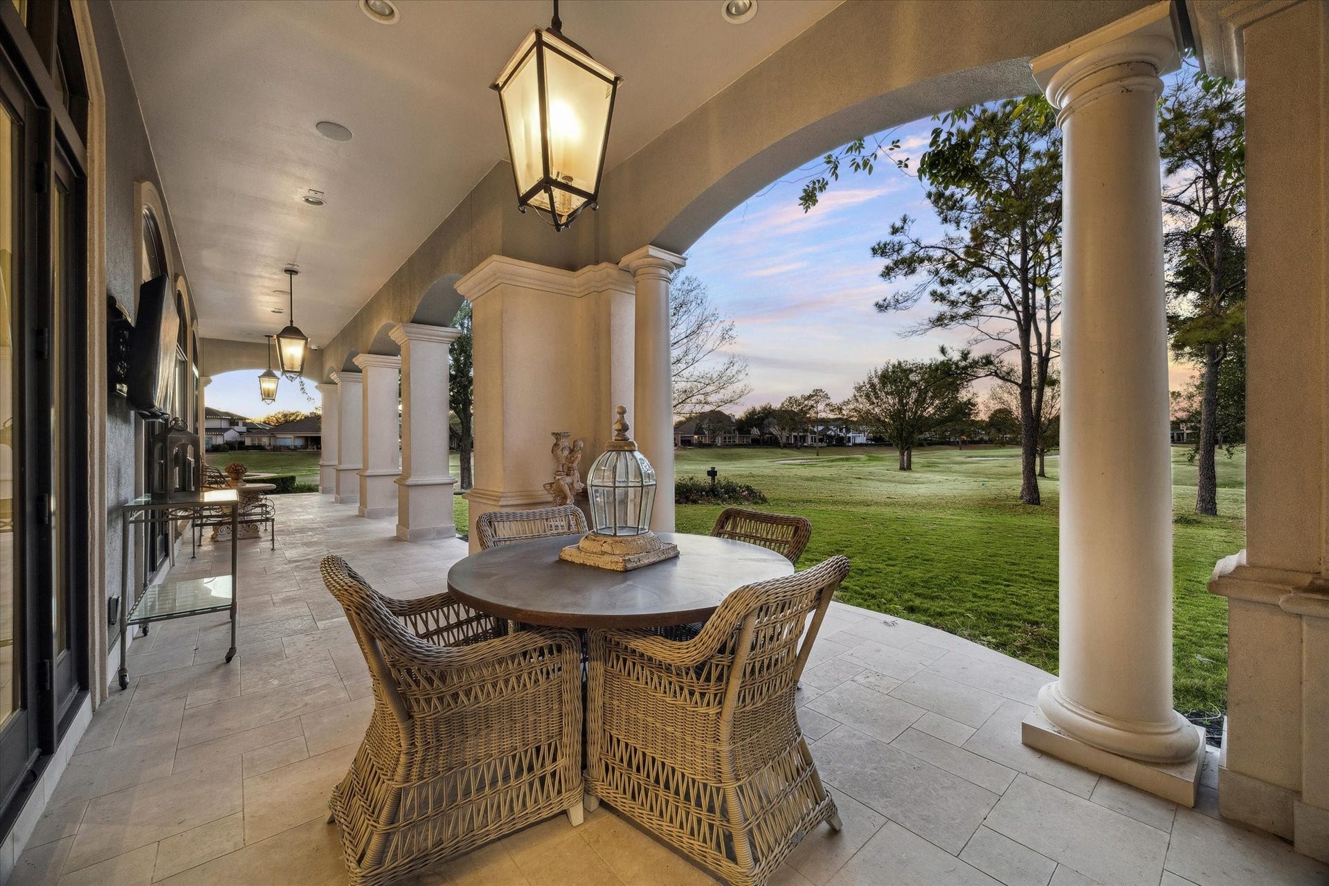 Expansive covered back patio featuring arched columns, stone flooring, and serene views of the golf course.
