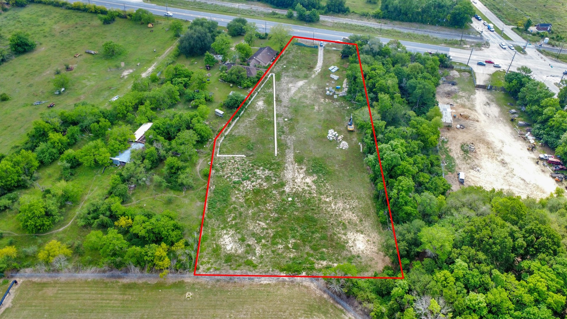 11826 Almeda Road, Houston, TX 77045 This photo shows a large, triangular plot of land outlined in red, featuring a mix of open grassy areas and scattered trees. It's adjacent to a road, offering easy access, with some nearby buildings and open spaces nearby, suggesting potential for development or agricultural use.