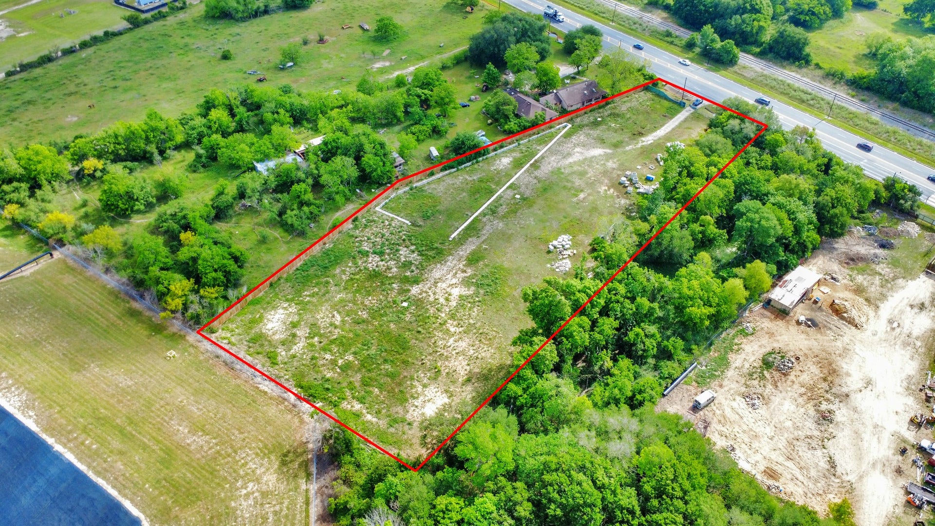 11826 Almeda Road, Houston, TX 77045 Expansive plot of land bordered by lush greenery, with a clear demarcation line. It features a house near a main road, offering easy access. Ideal for development or a private estate.