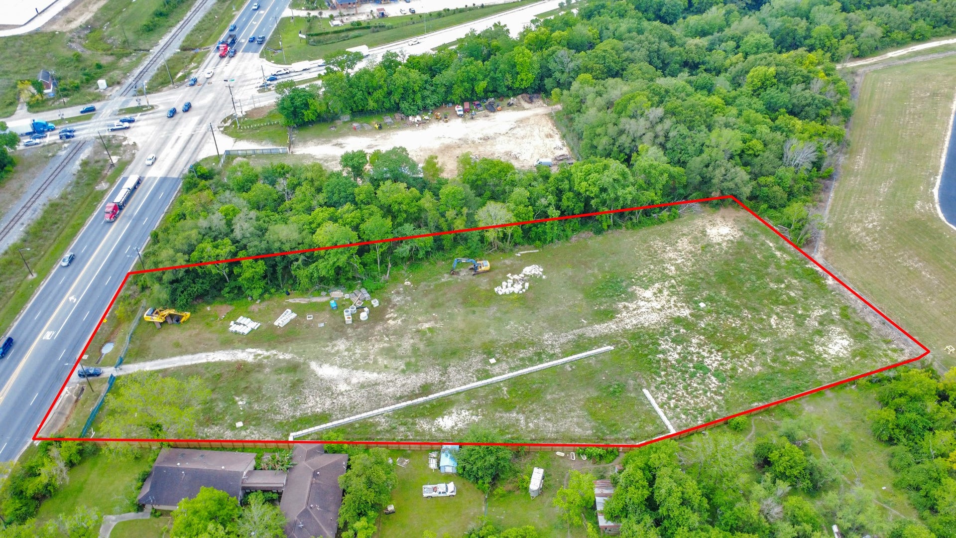 11826 Almeda Road, Houston, TX 77045 This aerial photo shows a large, triangular plot of land bordered by trees and a busy road on one side. The area is mostly open with some construction materials and machinery, suggesting potential for development. The plot is outlined in red, highlighting its boundaries.