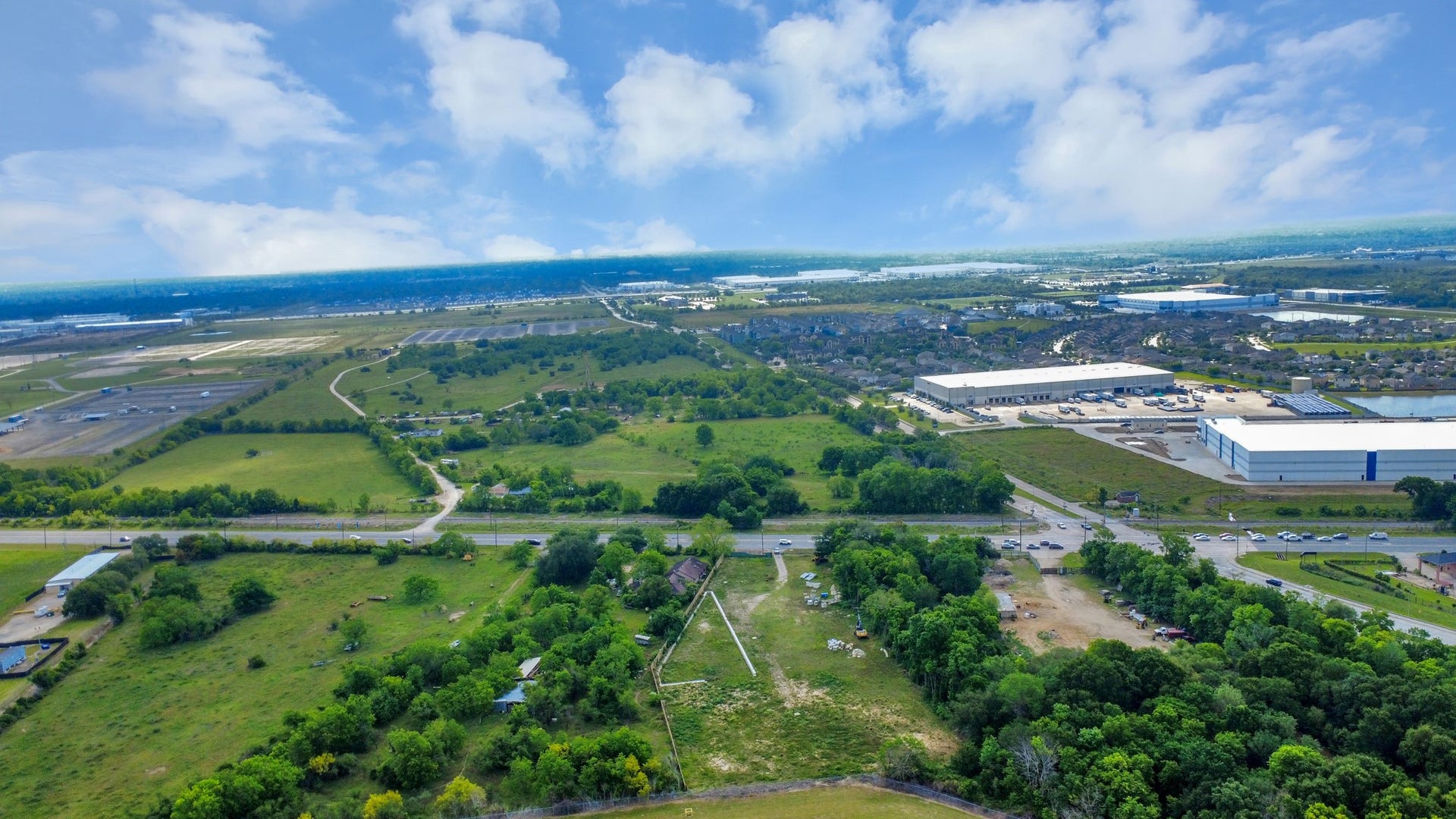 11826 Almeda Road, Houston, TX 77045 This aerial view showcases a vast, green landscape with scattered trees and open land, bordered by roads. In the distance, there are industrial buildings and a residential area, indicating a blend of rural and urban settings. Ideal for buyers seeking space with nearby amenities.