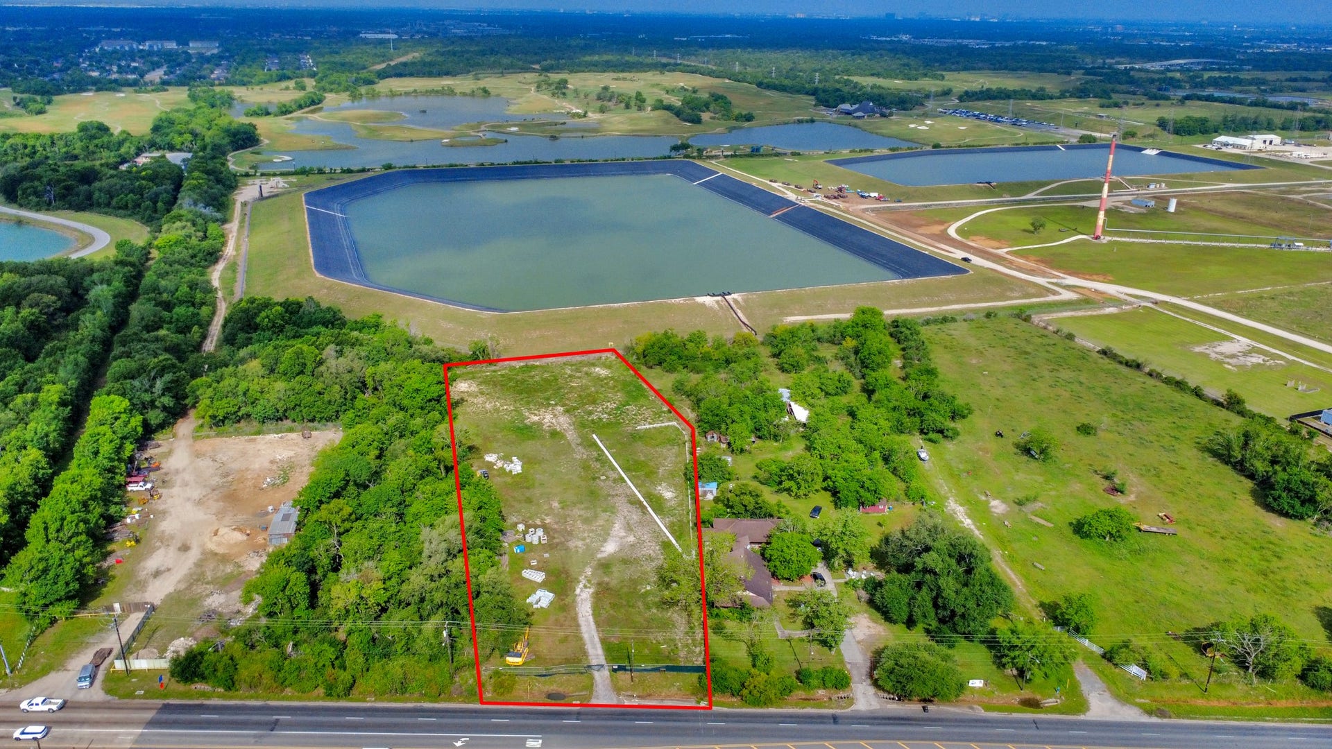 11826 Almeda Road, Houston, TX 77045 This aerial photo shows a large, rectangular plot of land outlined in red, situated next to a road. The surrounding area includes greenery, open fields, and several large water bodies, offering a spacious and scenic environment.