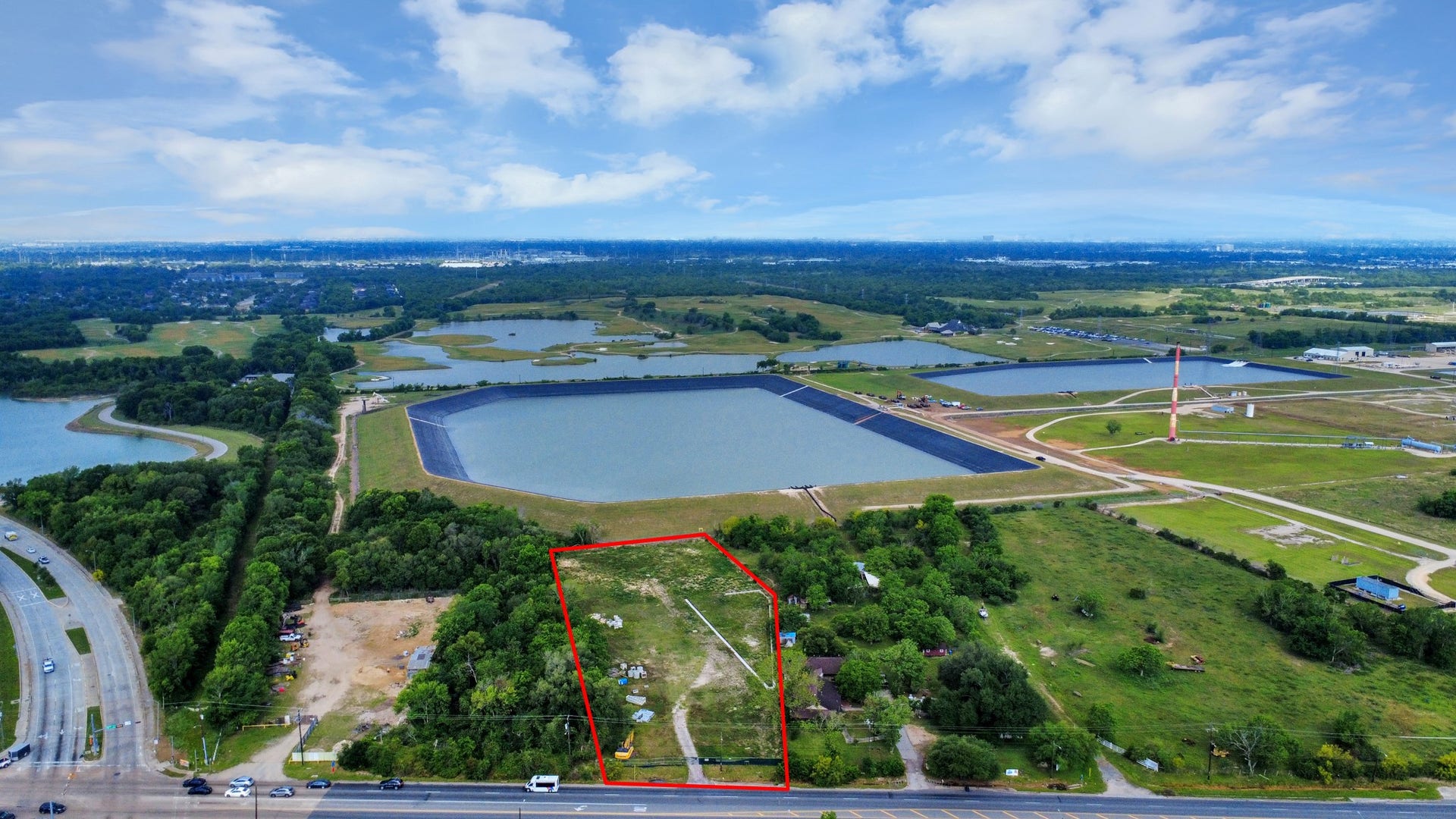 11826 Almeda Road, Houston, TX 77045 This aerial photo highlights a vast expanse of land outlined in red, surrounded by lush greenery and adjacent to large water bodies. The area has nearby roads and open spaces, offering a serene yet accessible location for potential development or home building.