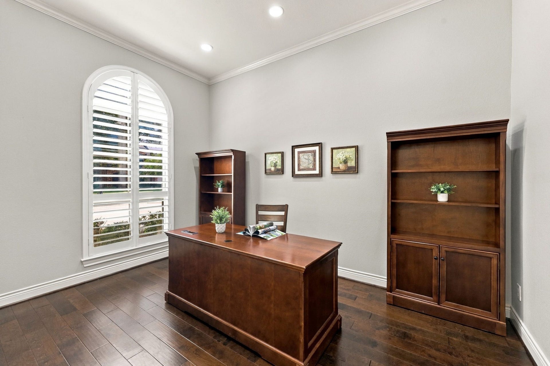 27302 Liberty Heights Lane, Fulshear, TX 77441 The Home Office features wide-plank wood flooring, an 11-foot ceiling, LED lighting, elegant crown molding, and 5-inch baseboards. A large arched window with plantation shutters adds architectural charm while allowing natural light to fill the space, creating a comfortable and private setting for working from home.