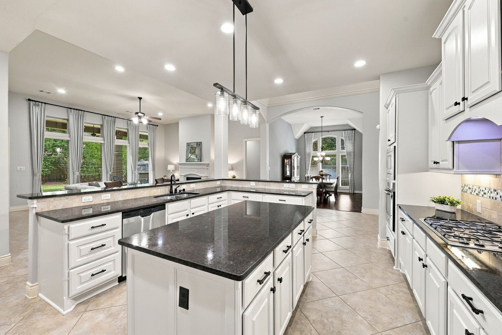 27302 Liberty Heights Lane, Fulshear, TX 77441 This view of the Kitchen looks back toward the Formal Dining Room and Family Room, highlighting the home's open and inviting layout. The large center island is beautifully accented by newly installed matte black pendant lights and coordinating cabinet hardware, adding a modern touch to the kitchen's timeless design.