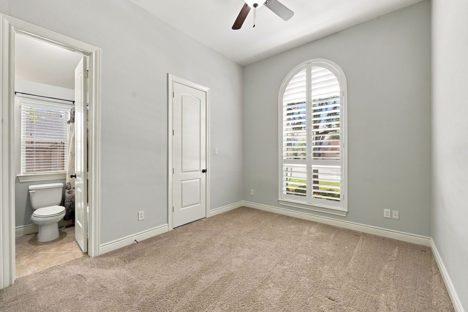 27302 Liberty Heights Lane, Fulshear, TX 77441 All Secondary Bedrooms are generously sized and feature walk-in closets and direct access to a Bathroom. This Bedroom is located at the front of the home and features a large arched window with plantation shutters, soft, light-colored walls, and wall-to-wall carpeting, creating a bright and comfortable space.
