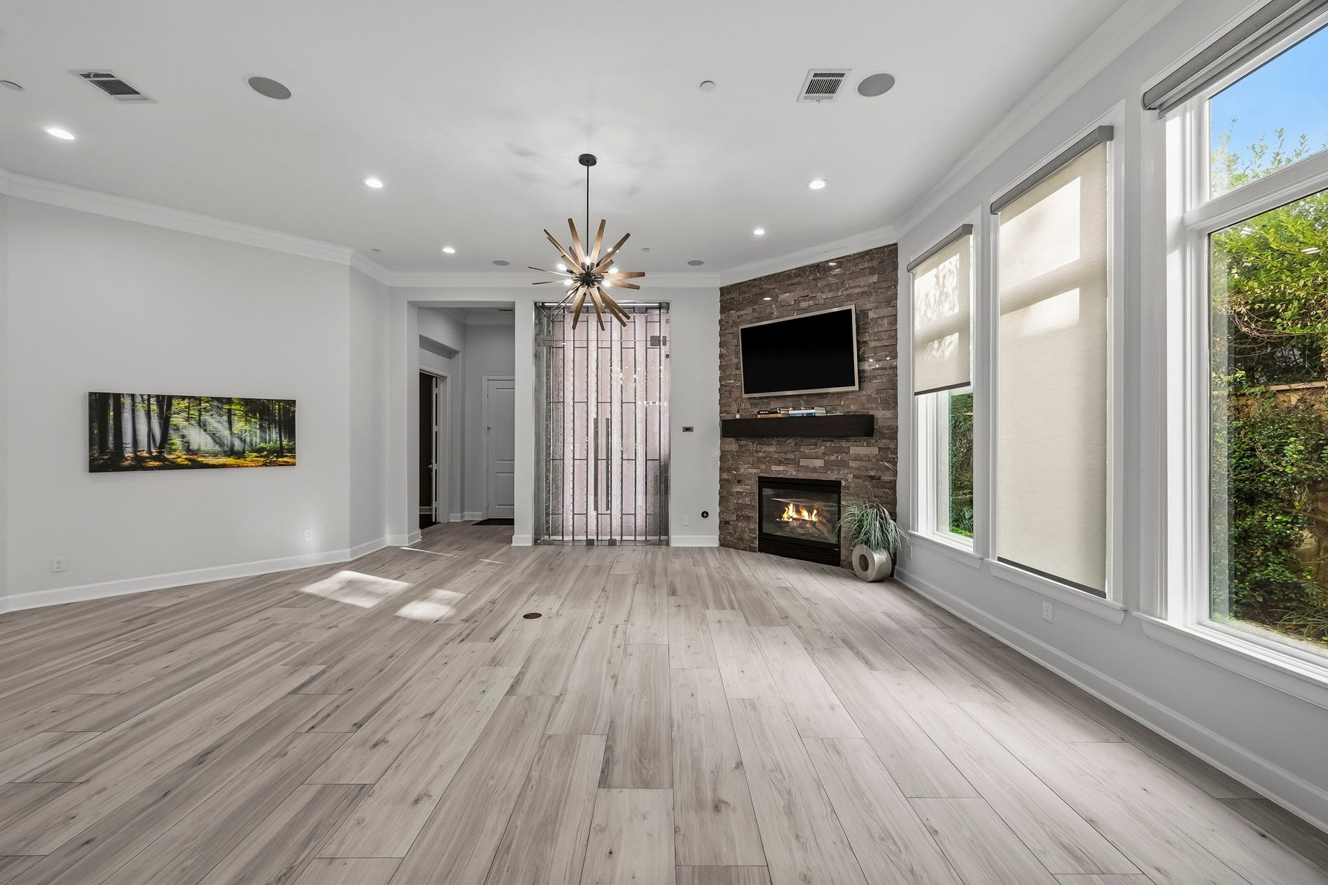 Spacious living room featuring elegant flooring, a cozy fireplace with a stone accent wall, and abundant natural light streaming through large windows.