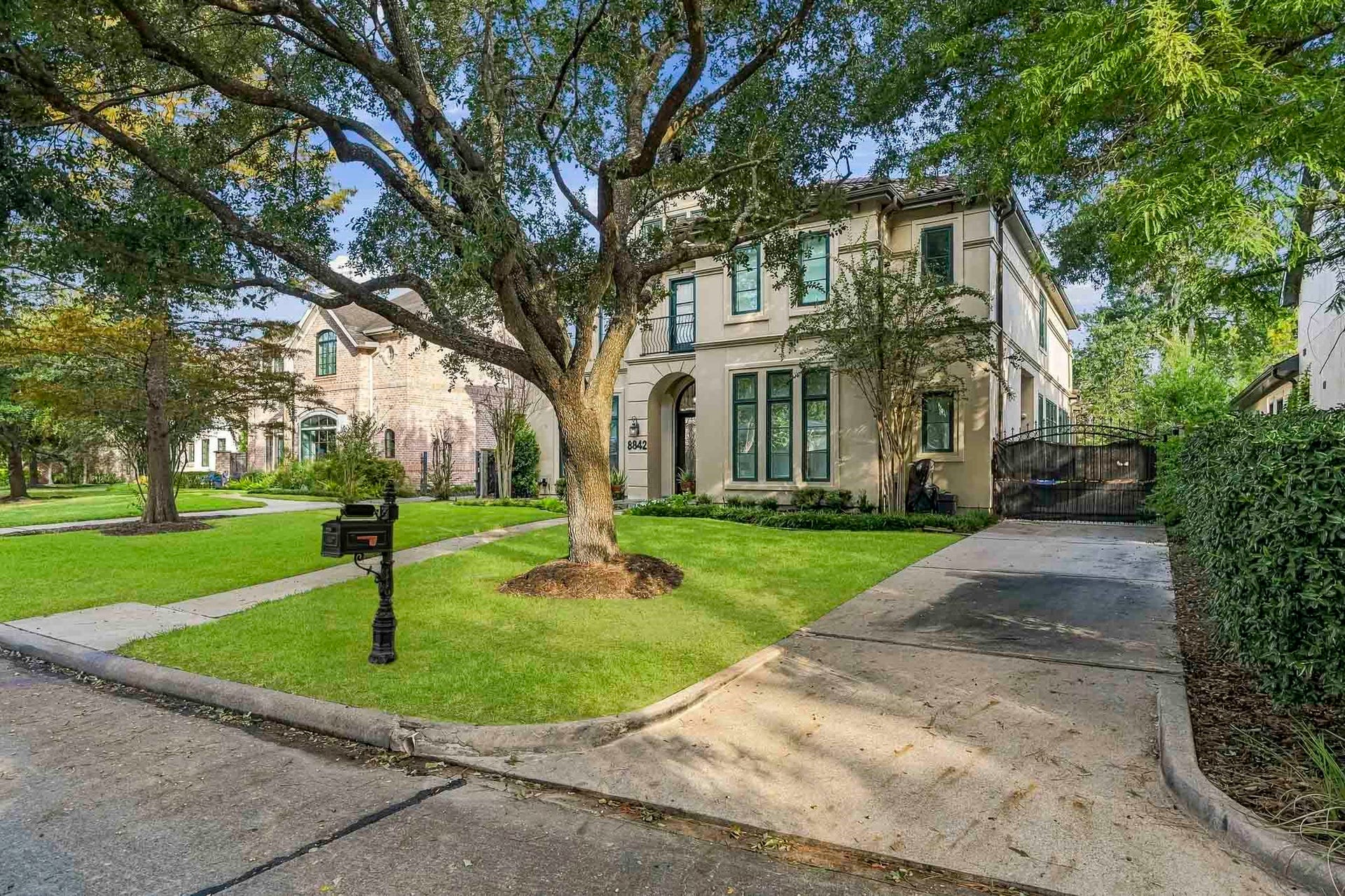 Elegant two-story home with a classic facade, framed by mature trees and lush landscaping, offering a welcoming driveway and charming curb appeal.