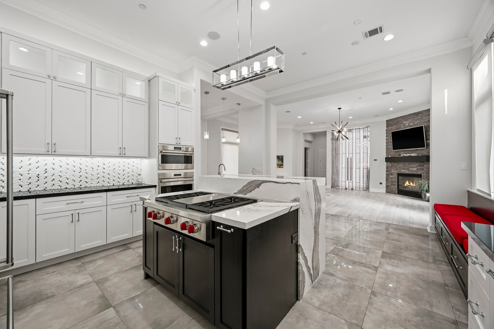 Modern kitchen featuring sleek white cabinetry, a stylish backsplash, and a spacious island with high-end appliances. The open layout flows into a cozy living area with a fireplace and ample natural light.