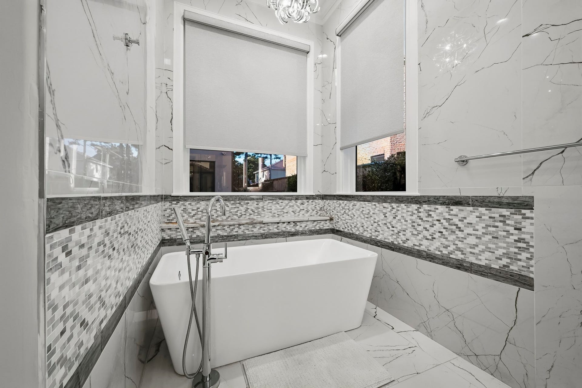 Luxurious primary bathroom featuring a modern freestanding tub, elegant walls, and stylish mosaic accents, creating a serene spa-like atmosphere.