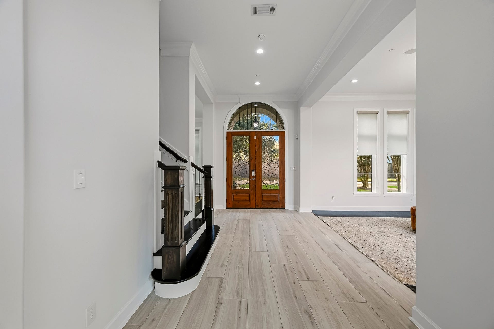 Stunning entryway featuring elegant flooring, a grand arched door, and abundant natural light streaming through large windows, creating a welcoming and sophisticated atmosphere.