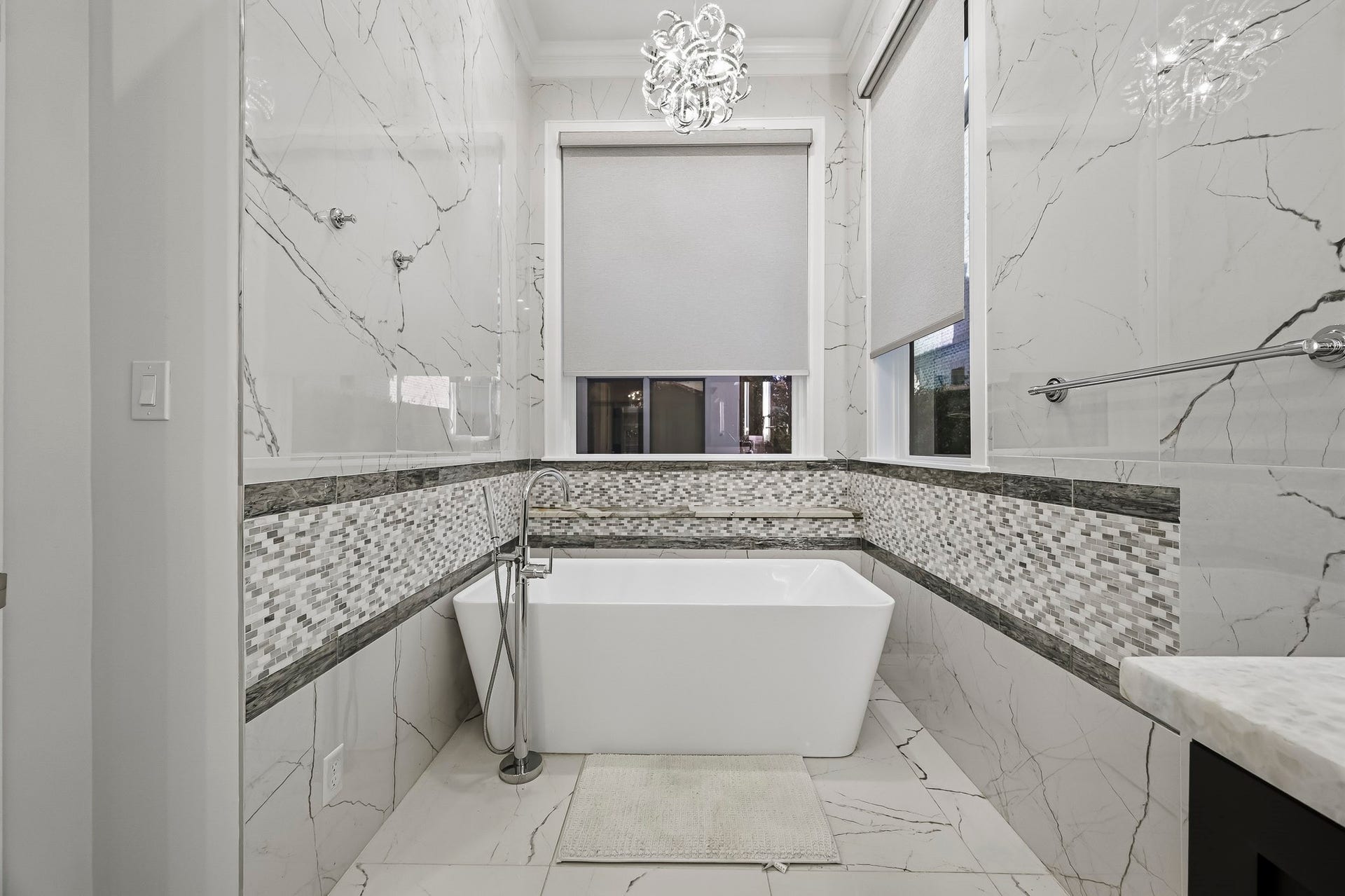 Luxurious bathroom featuring a sleek freestanding tub, and chic mosaic tile accents, all illuminated by a stunning modern chandelier.