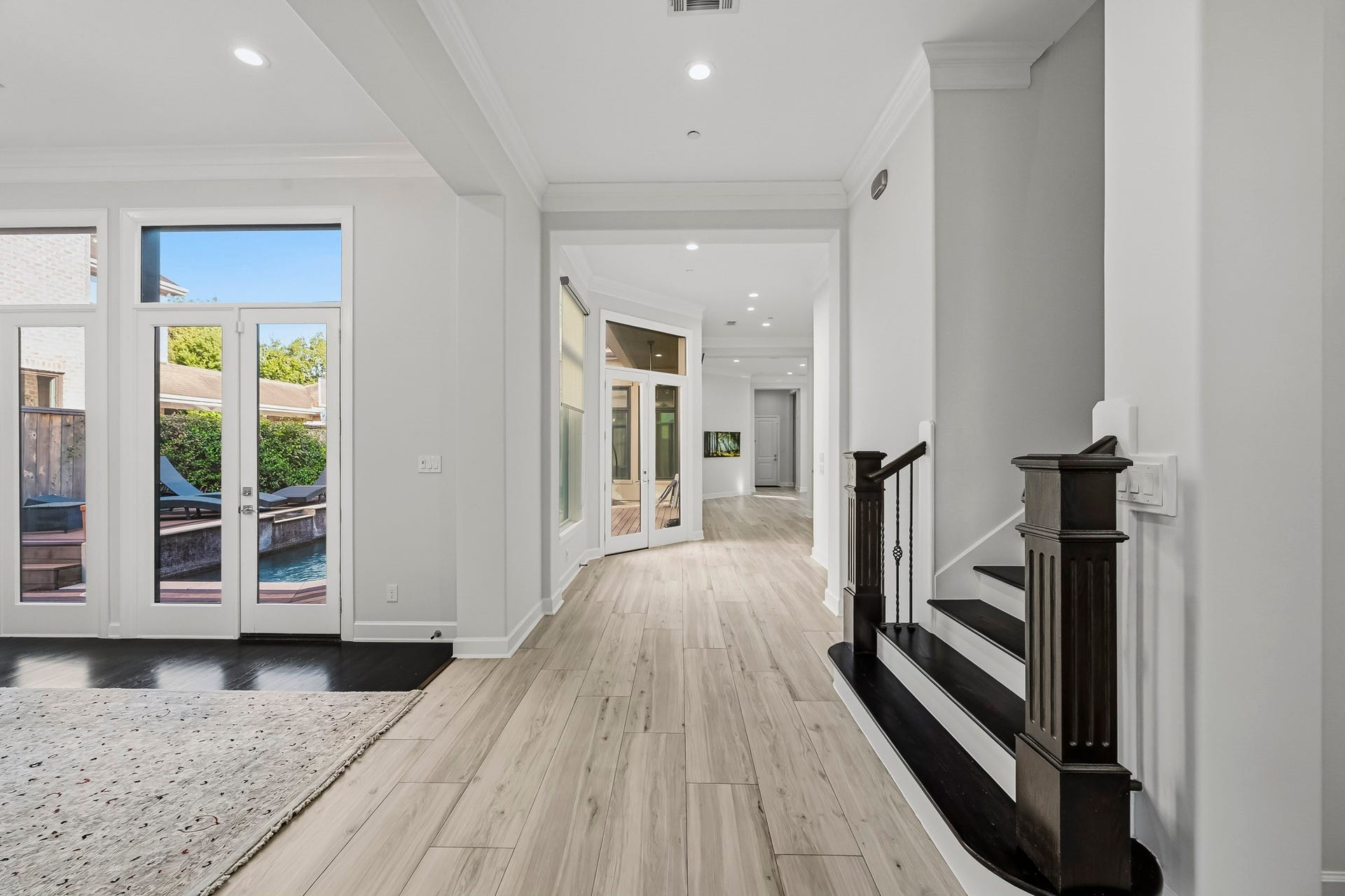 Elegant entryway with sleek floors leading to an open living space. French doors offer abundant natural light and a view of the inviting outdoor pool area.