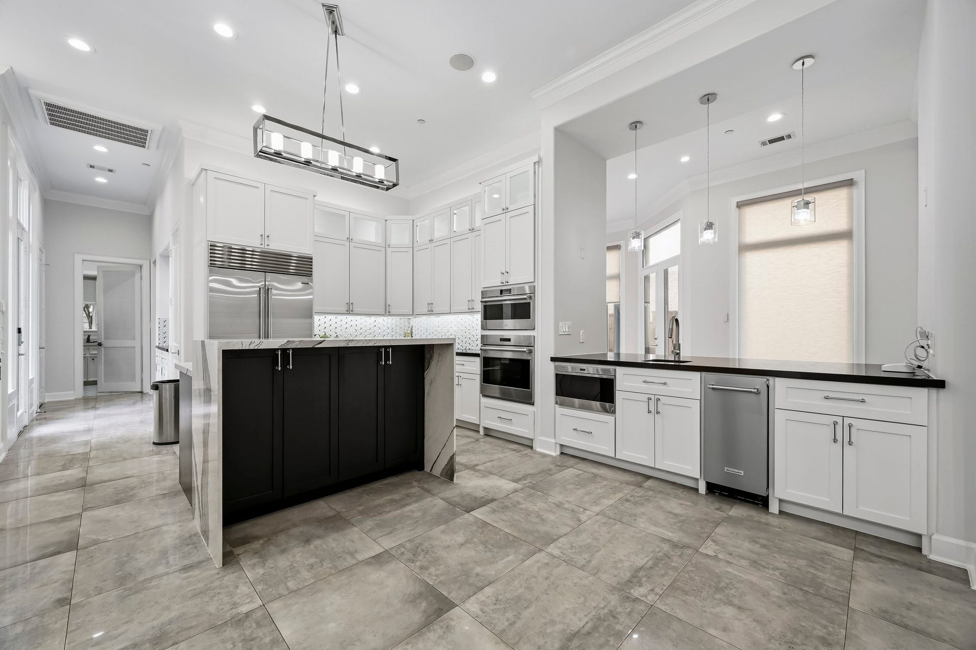 A modern kitchen featuring cabinetry, high-end stainless steel appliances, and elegant pendant lighting, complemented by a spacious island and polished tile flooring.