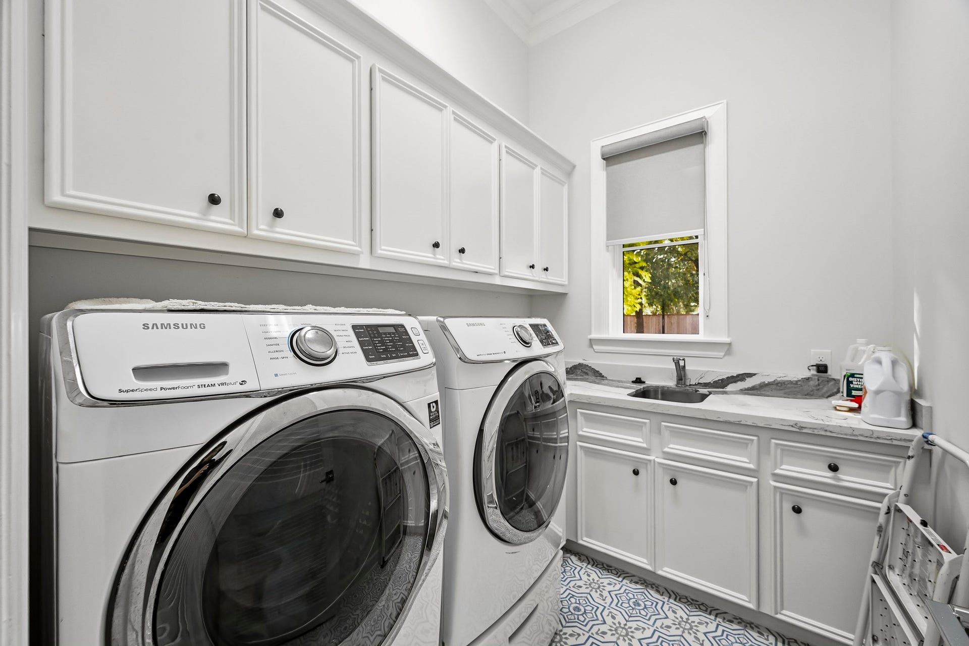 Spacious laundry room featuring modern washer and dryer, ample cabinetry, and a convenient sink area with a view.