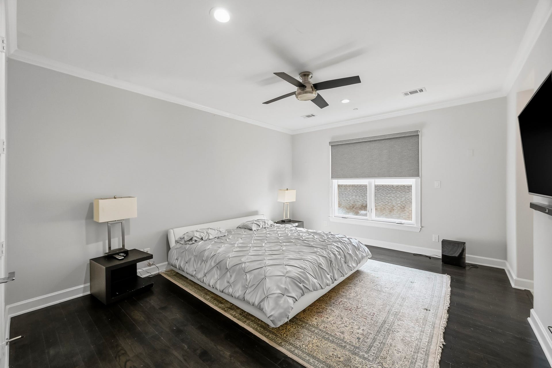 Spacious secondary bedroom with sleek dark floors, modern ceiling fan, and ample natural light from a large window.