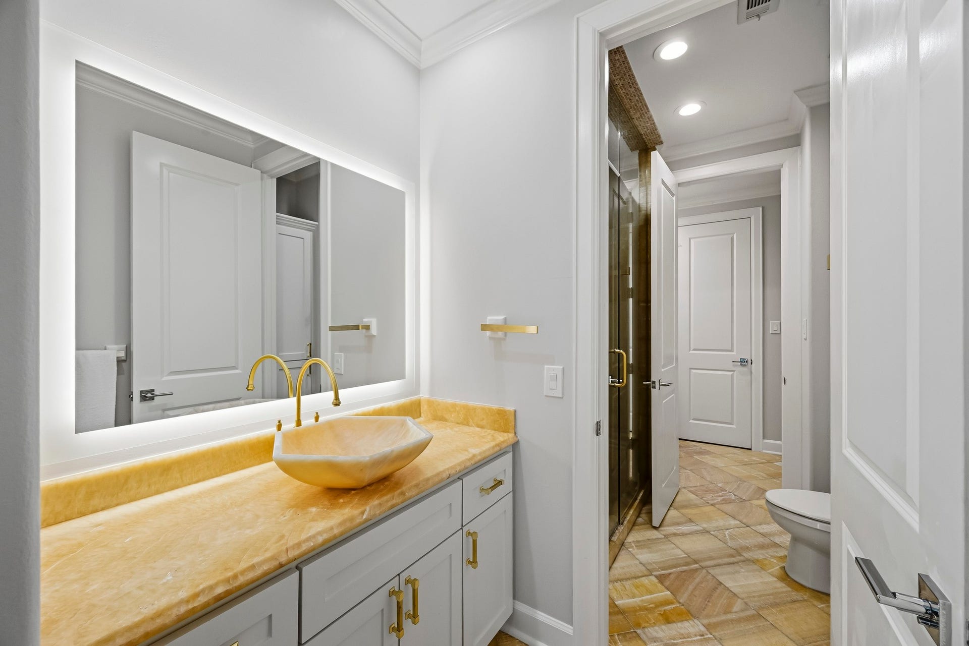Elegant jack and jill bathroom featuring a luxurious vessel sink with a stylish gold faucet, a glowing backlit mirror, and sophisticated tile flooring.