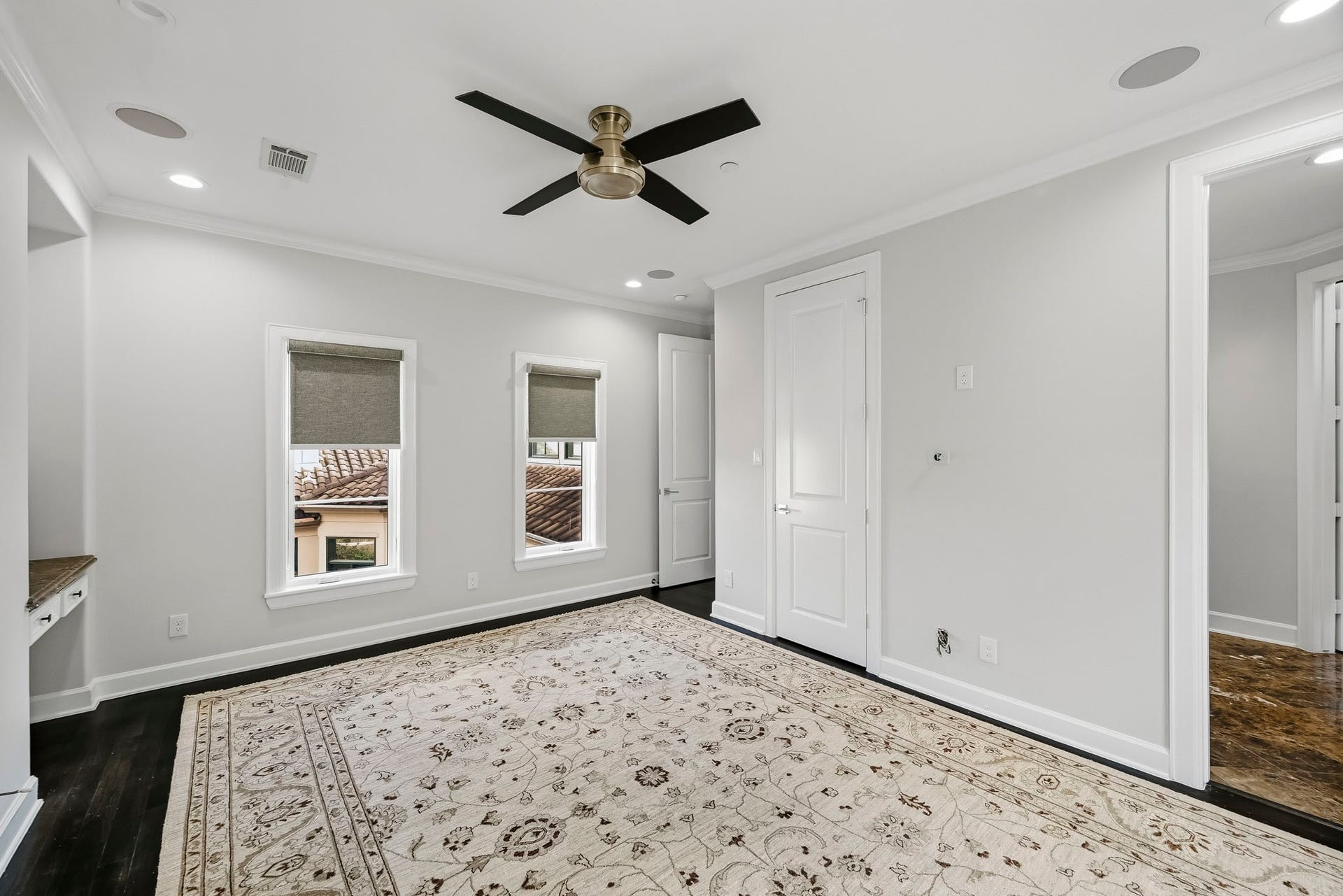 Bright and airy bedroom with elegant dark flooring, a stylish ceiling fan, and ample natural light from two windows.